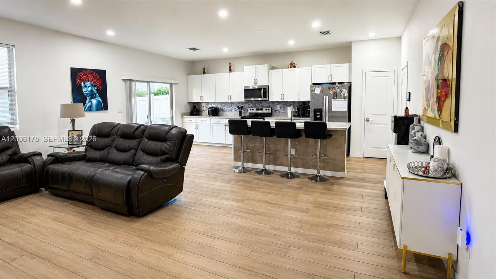 Open-concept kitchen featuring white shaker-style cabinetry, stainless steel appliances, a quartz-topped island with breakfast bar seating, recessed lighting, and wood-finish tile flooring
