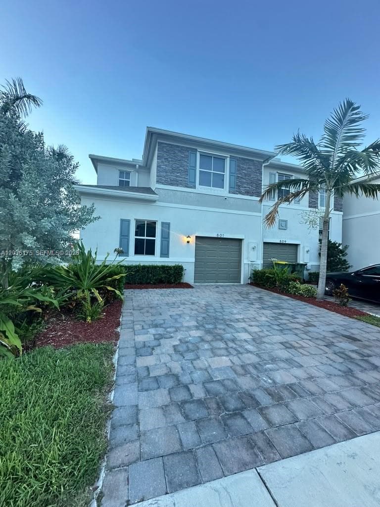 Two-story exterior featuring a stone-veneer accent wall, paver driveway, attached garage, and decorative shutters