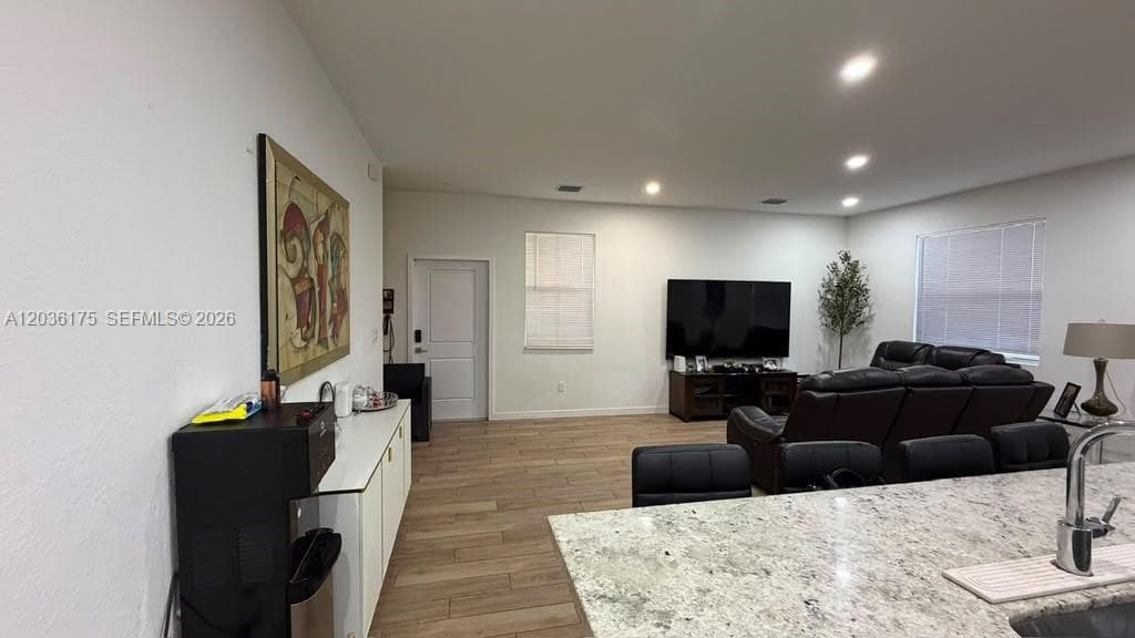 Open-concept space featuring wood-finish tile flooring, recessed lighting, and a kitchen island with stone-surface countertop and integrated stainless steel sink