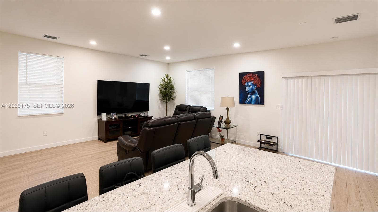 Interior space featuring light-toned wood-finish flooring, recessed lighting, expansive island with stone-finish countertop, under-mount stainless steel sink, and sliding glass door