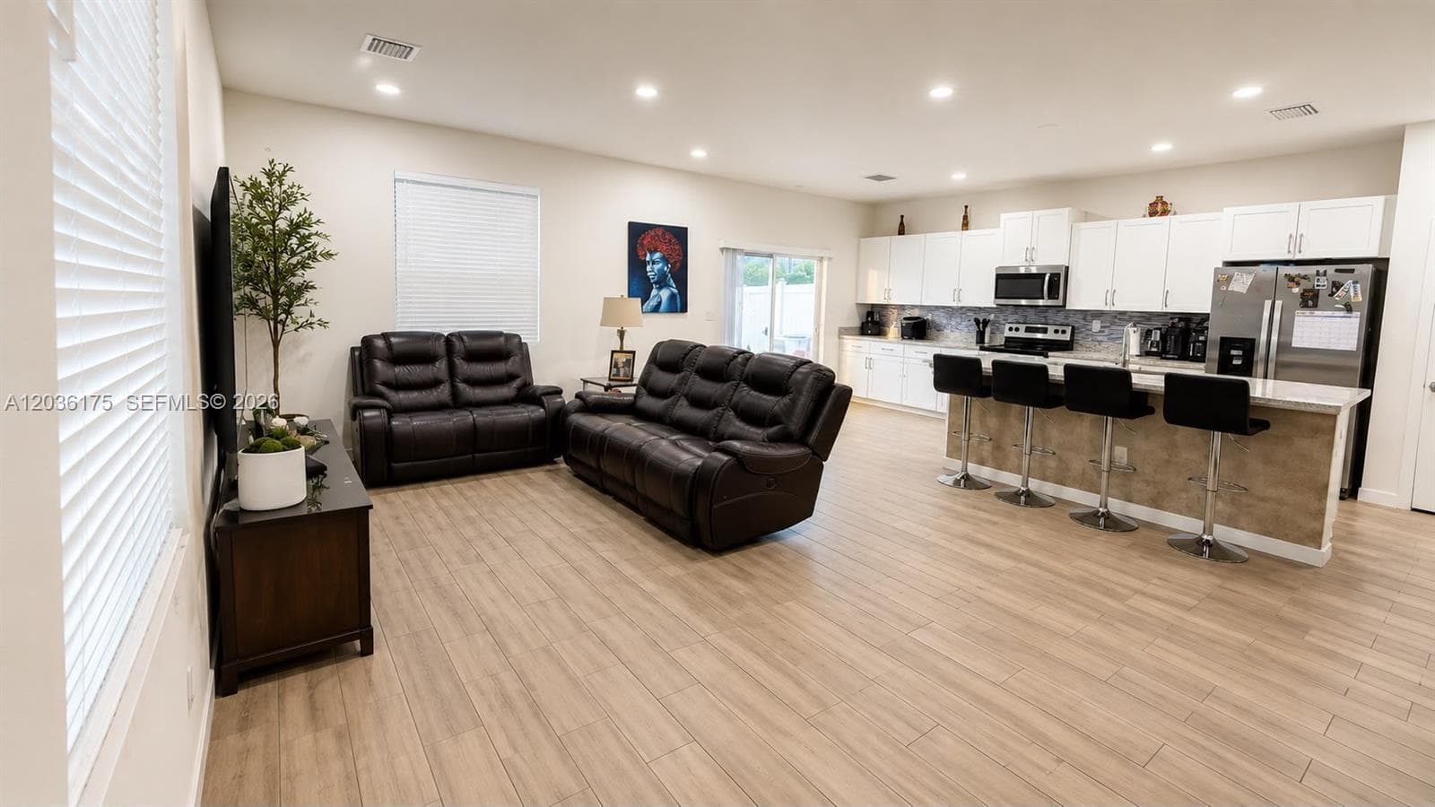 Open-concept floor plan featuring wood-finish tile flooring, recessed lighting, white cabinetry, a center island with bar seating, and stainless steel kitchen appliances