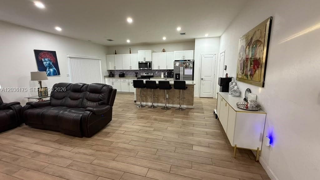 Kitchen featuring white cabinetry, an island with stone-finish base, stainless steel appliances, and recessed lighting, all complemented by wood-finish flooring