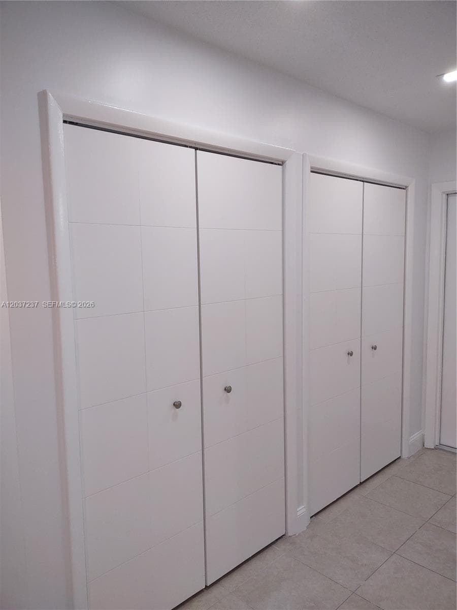 Dual sets of white, multi-panel bi-fold doors featuring minimalist round hardware, complemented by light-toned neutral tile flooring