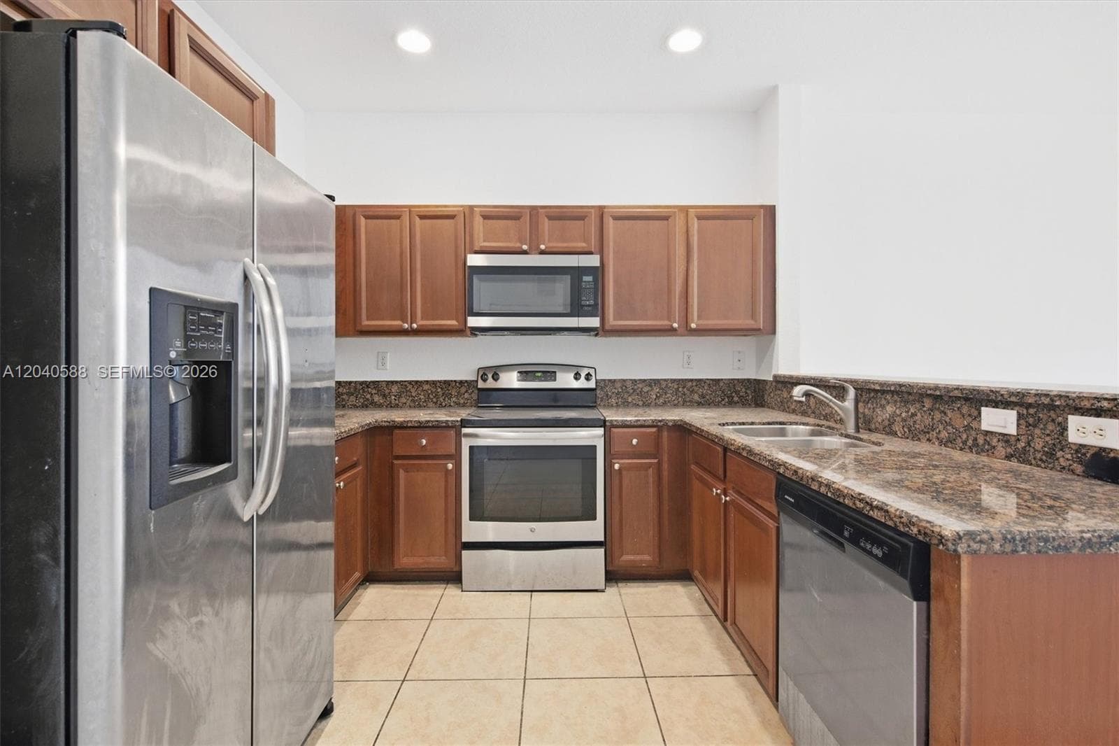 Kitchen featuring stainless steel appliances, wood-finish cabinetry, stone countertops, and tile flooring
