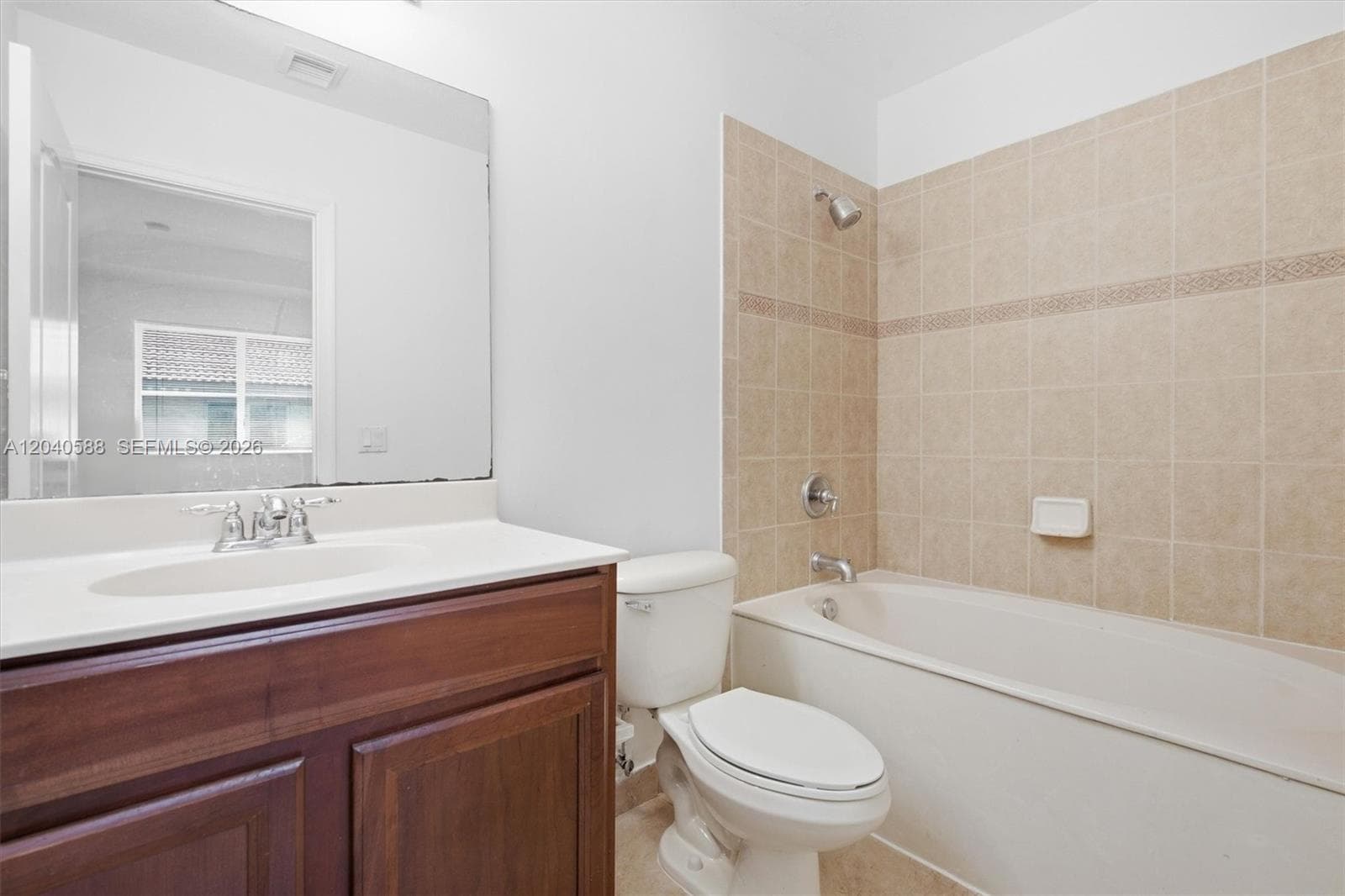 Full bathroom featuring a wood-finish vanity with an integrated sink, a large wall-mounted mirror, a toilet, and a shower-tub combination with tiled walls and an accent border