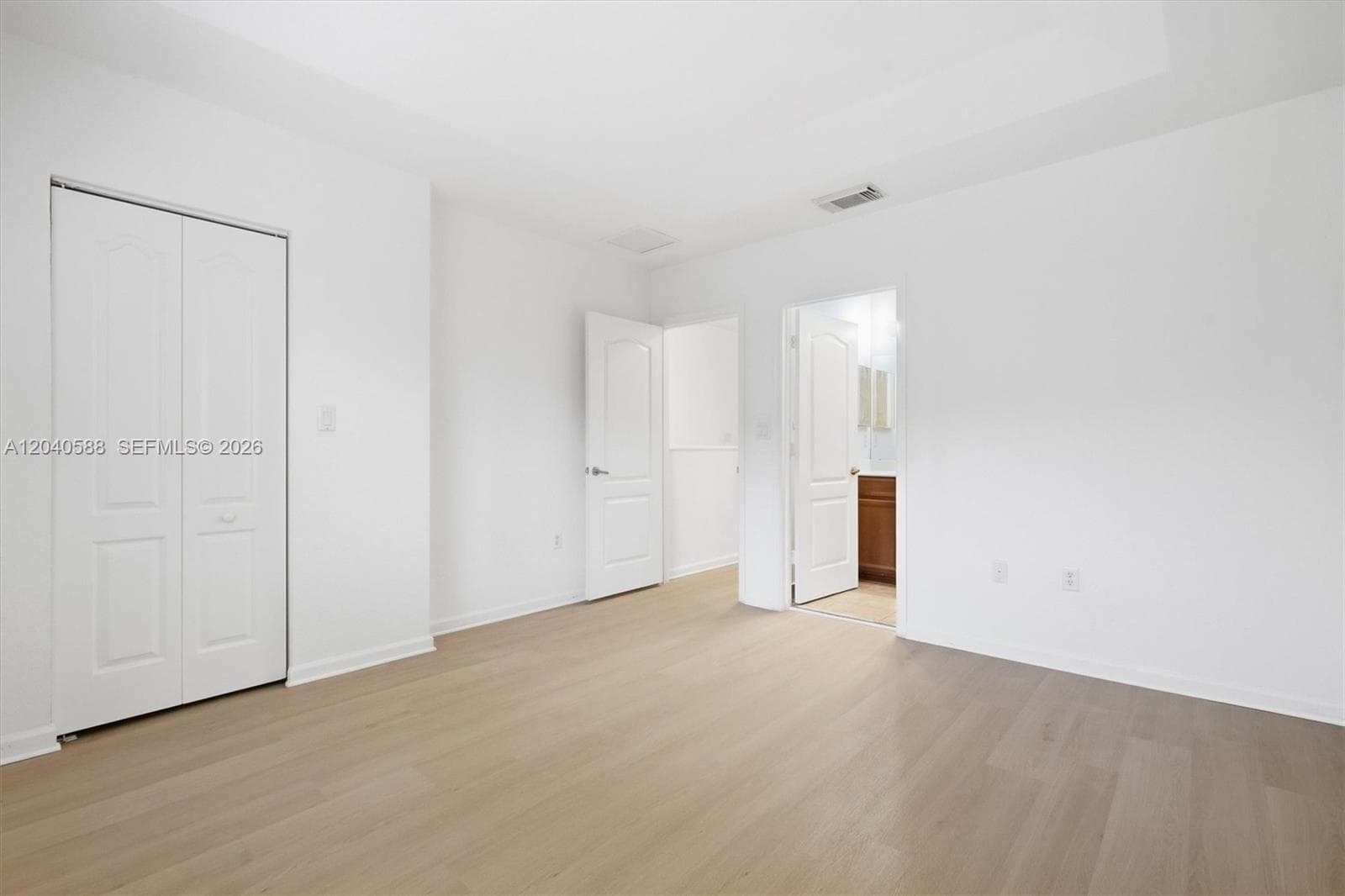 Spacious room featuring wood-finish flooring, white walls, and bright overhead lighting