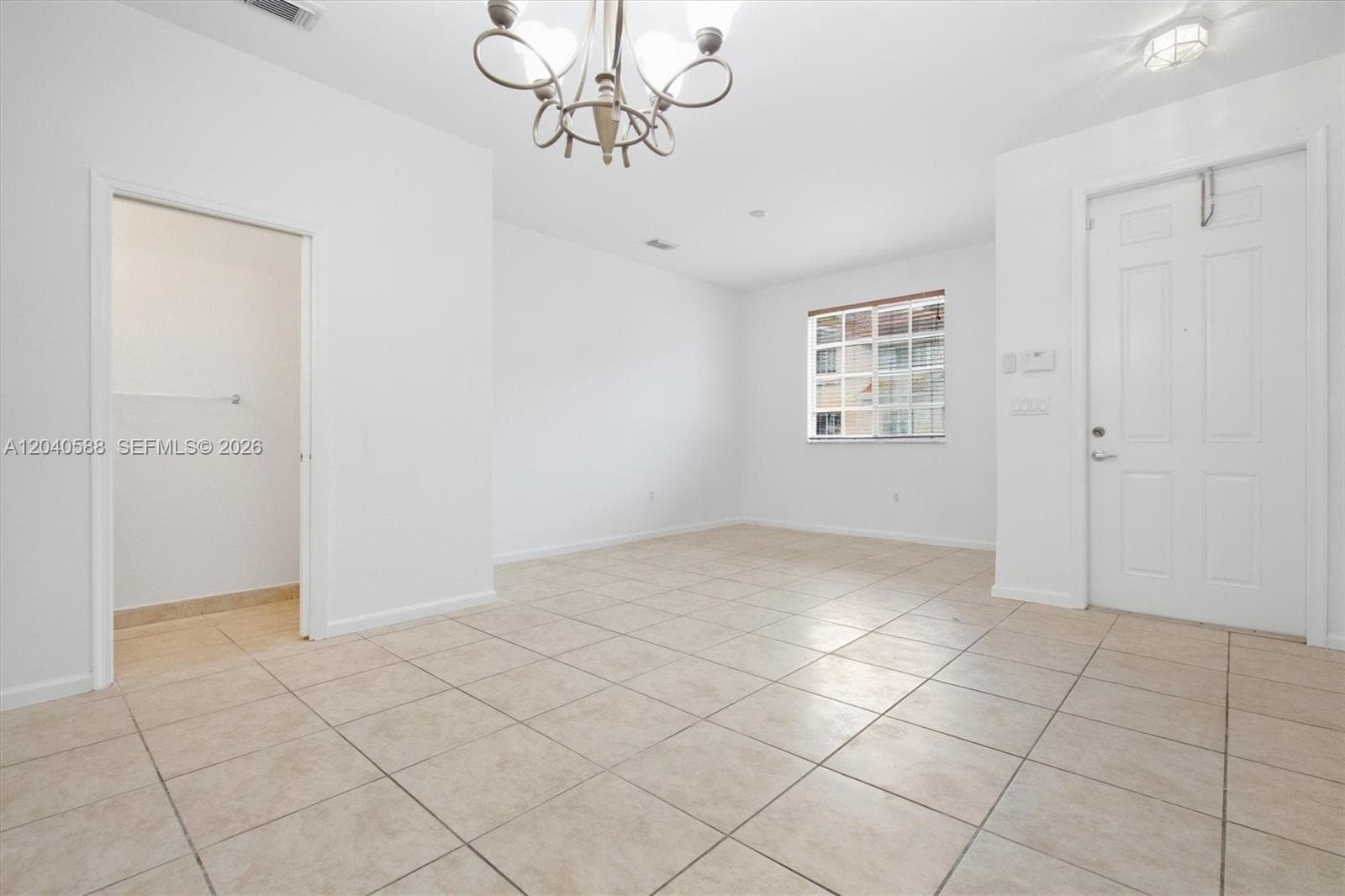 Beige tile flooring, window with grid panes, white paneled door, built-in closet, and a chandelier fixture