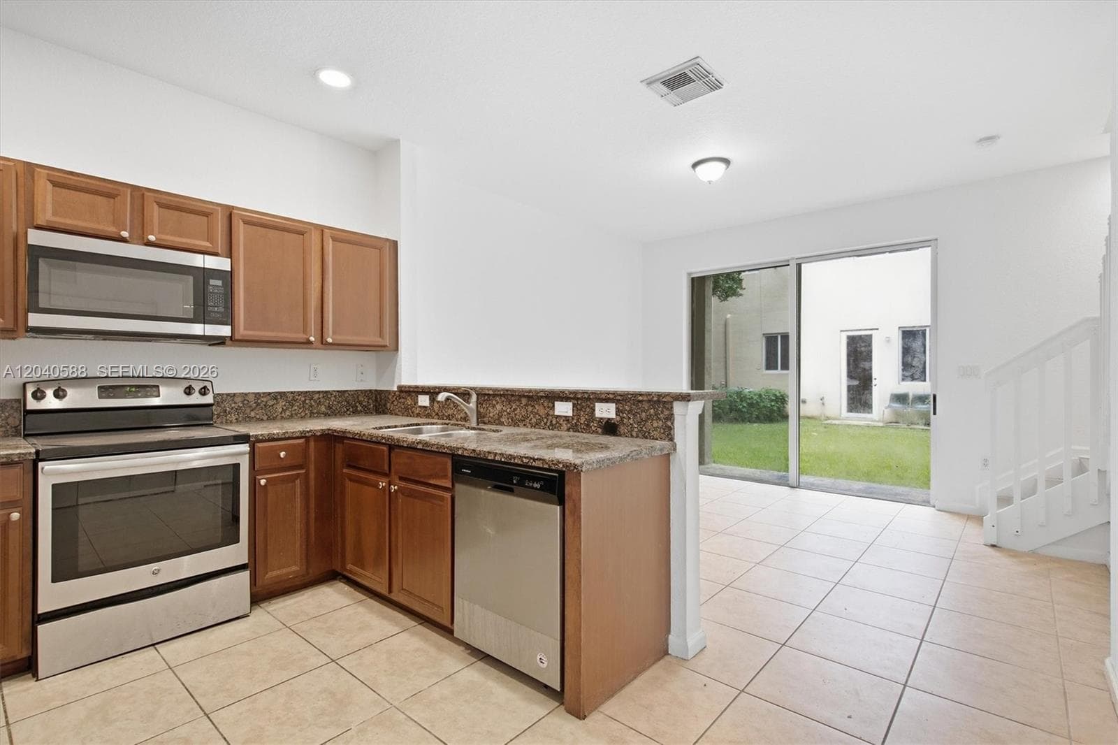 Kitchen featuring stainless steel appliances, wood cabinetry, stone countertops, and tile flooring