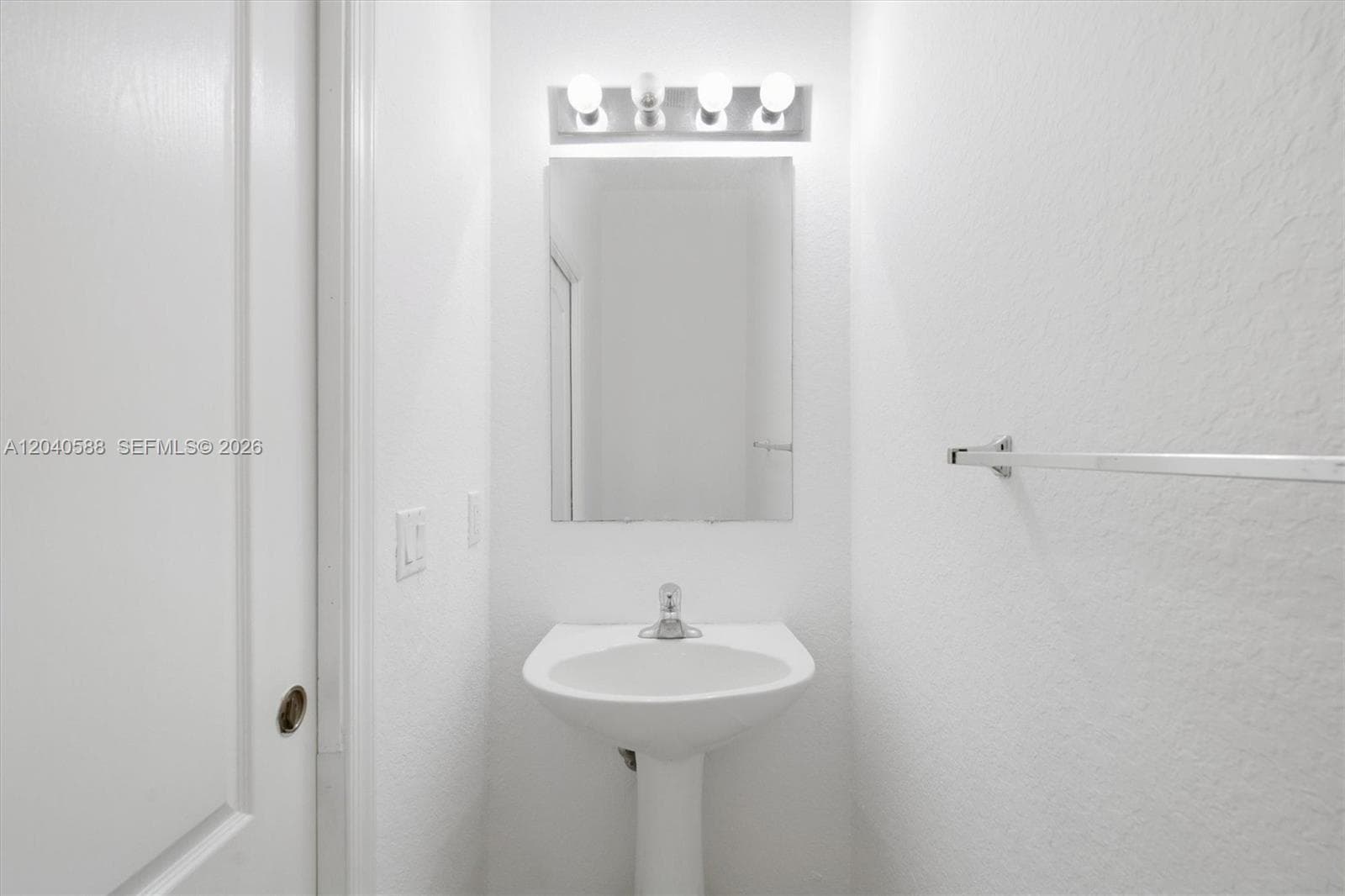 Pedestal sink with chrome-finish faucet, wall-mounted mirror, and vanity light fixture