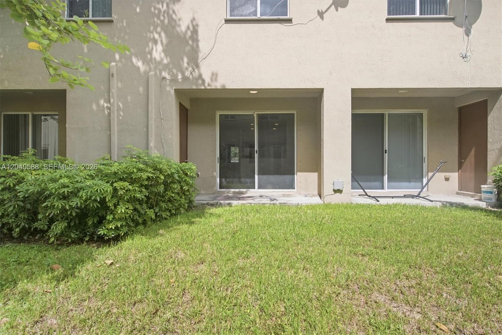 Expansive green lawn with mature shrubbery, featuring two sets of sliding glass doors and a private patio space