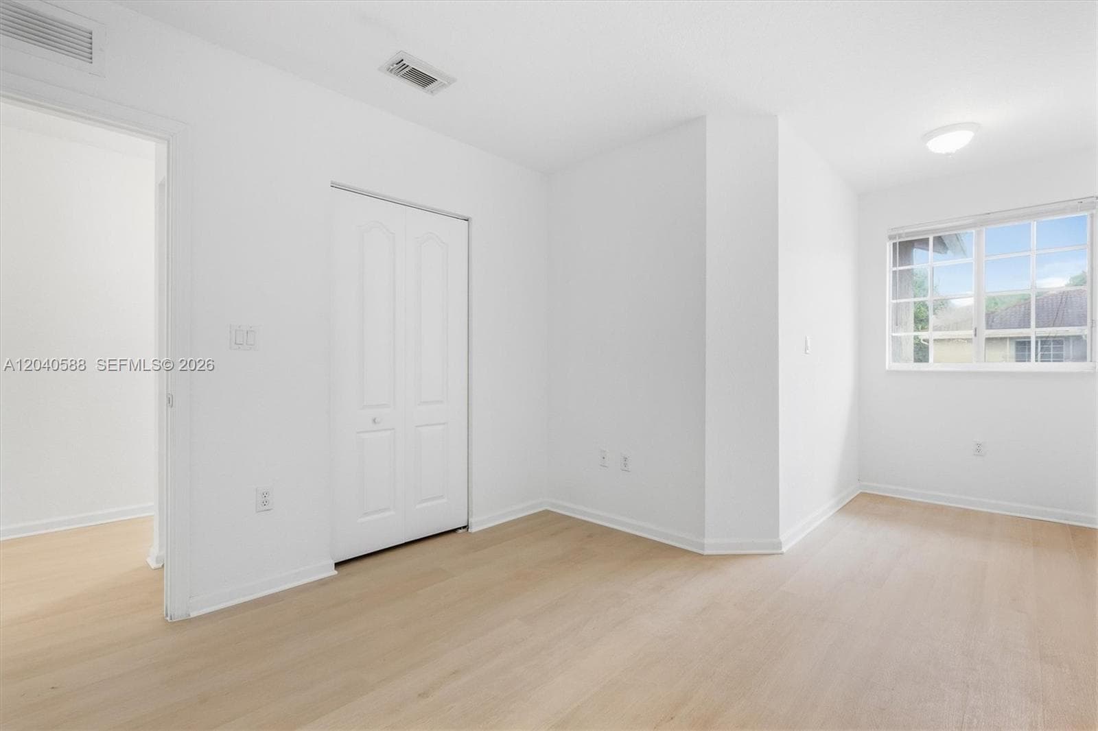 White walls, wood-finish flooring, bi-fold closet doors, recessed ceiling lighting, and a large window