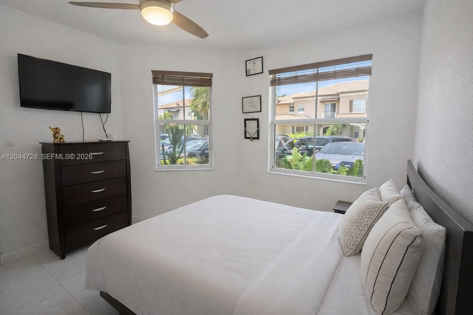 Bright bedroom with clean tile flooring, clean layout,  and modern ceiling fan. Well-kept space with natural light.
