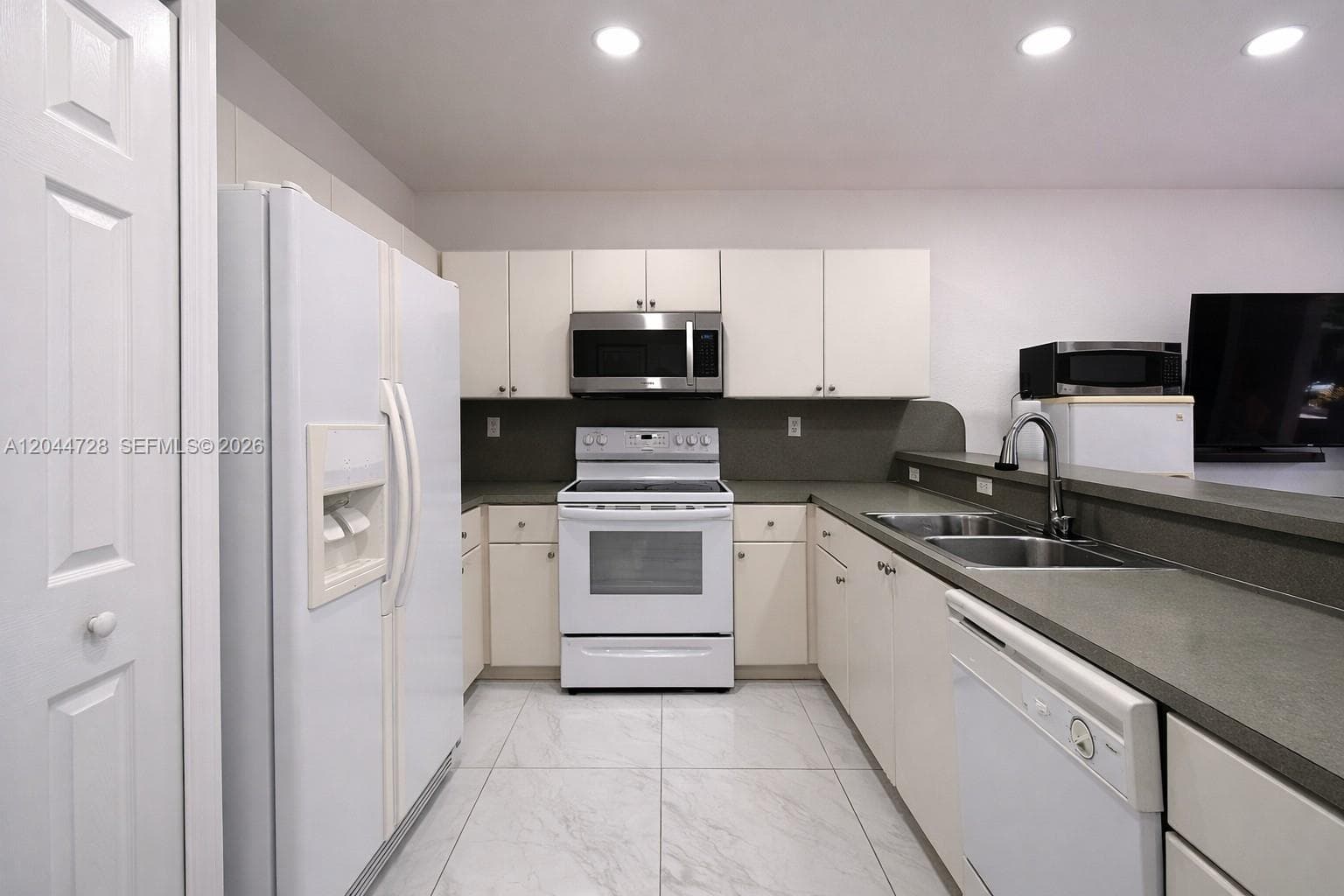 Bright and clean kitchen with white cabinetry, and spacious tile flooring. Functional layout with ample counter space and a fresh, well-maintained look.