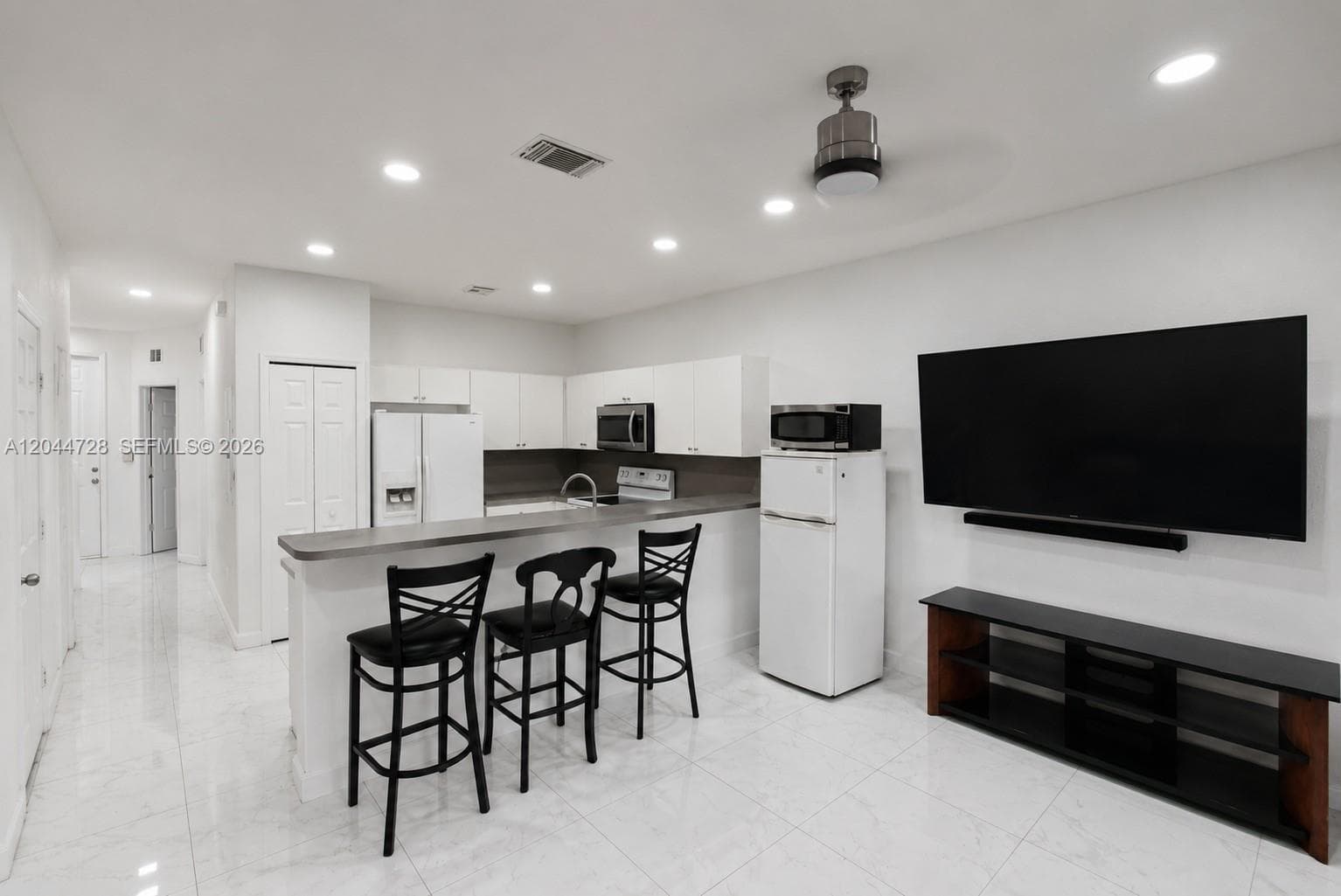 Bright open kitchen and living area with white appliances, and clean tile flooring. Clean, functional layout with a contemporary feel.