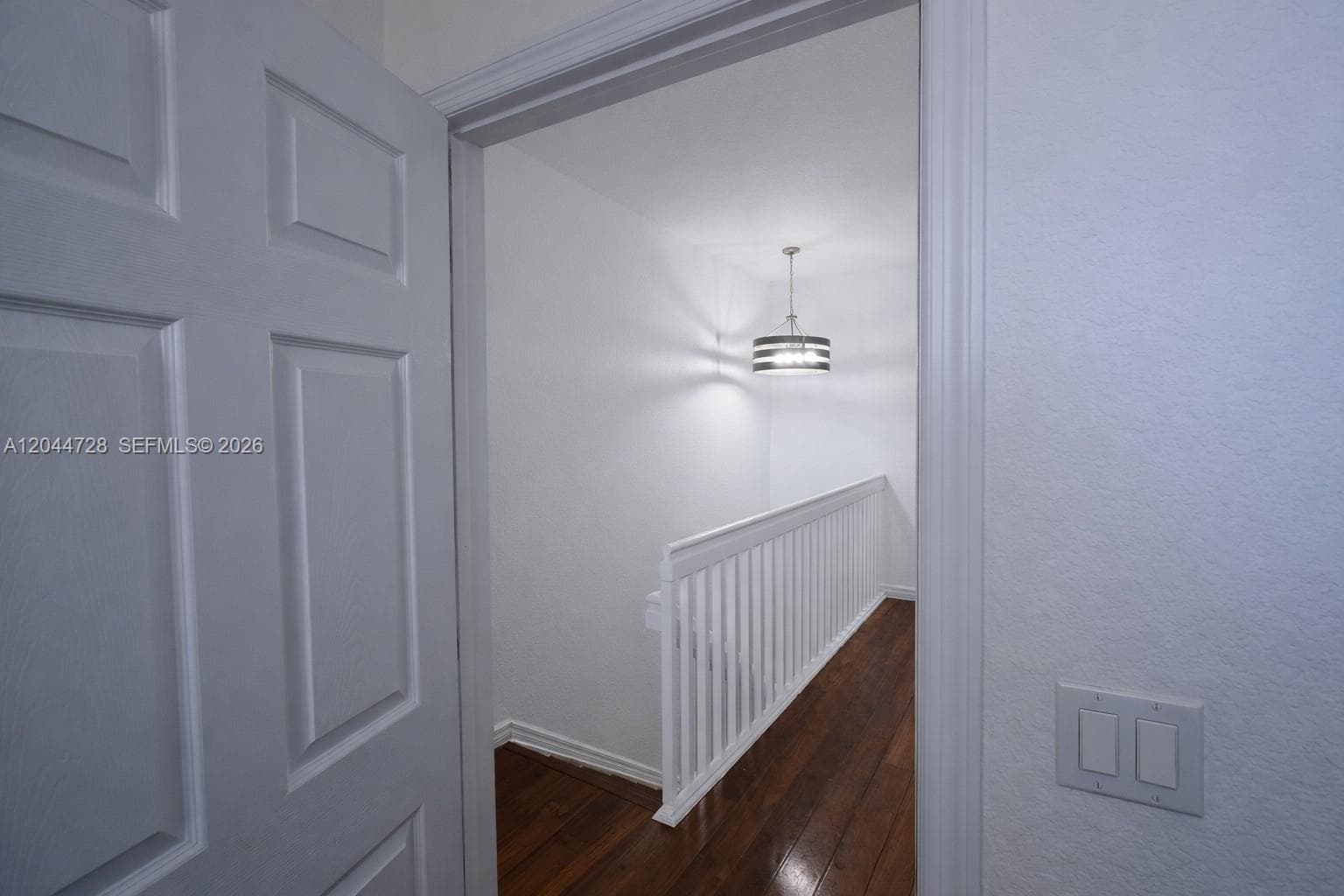 Clean hallway with white walls, laminated flooring, and modern light fixture. Features a sleek staircase and multiple doors for convenient access.