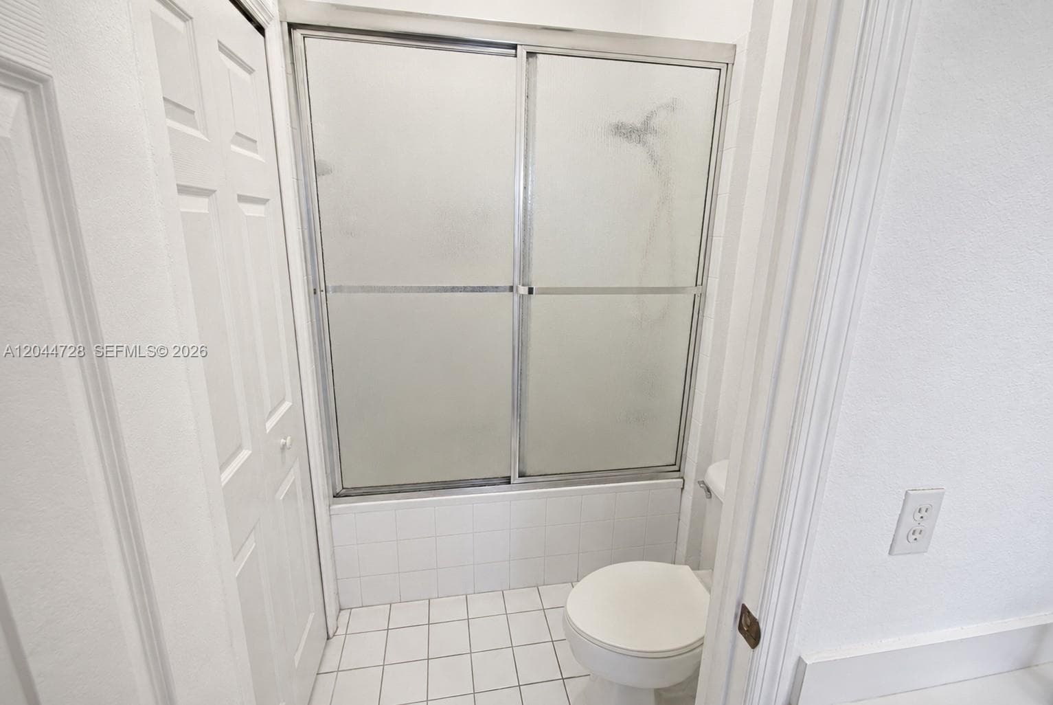 1st Master Bathroom with white tile flooring, tub with sliding glass doors, and a simple, functional layout