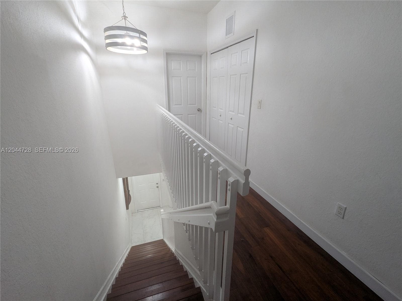 Clean hallway with white walls, laminated flooring, and modern light fixture. Features a sleek staircase and multiple doors for convenient access.