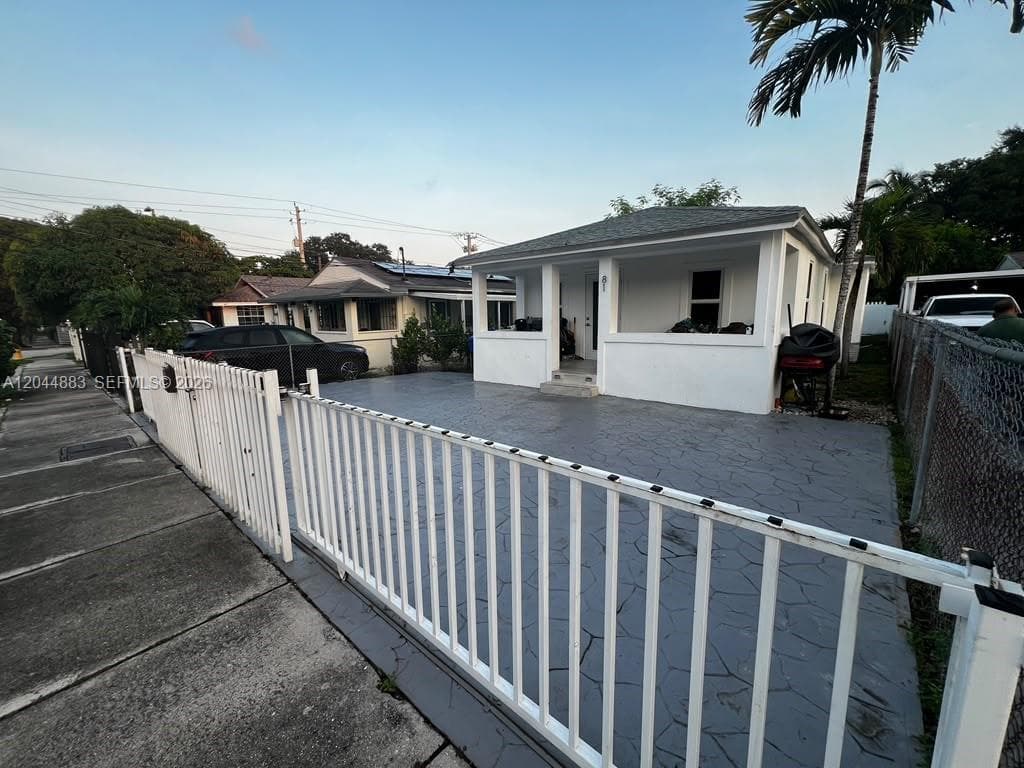Exterior of a single-story residence featuring a covered front porch, stamped concrete driveway, and white metal perimeter fencing