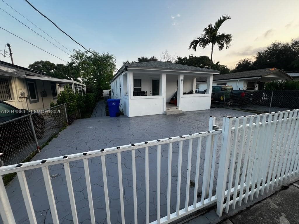 Single-story residence featuring a covered front porch, exterior paint finish, and paved off-street parking area enclosed by a metal fence
