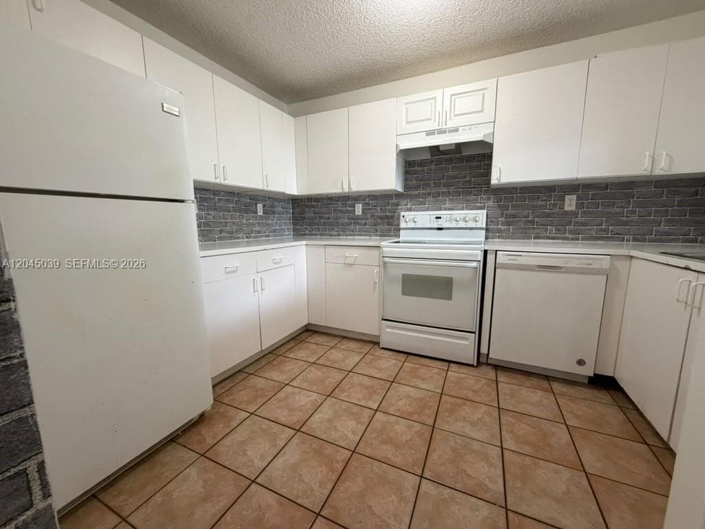 Kitchen featuring white cabinetry, textured tile backsplash, ceramic tile flooring, and integrated white appliances