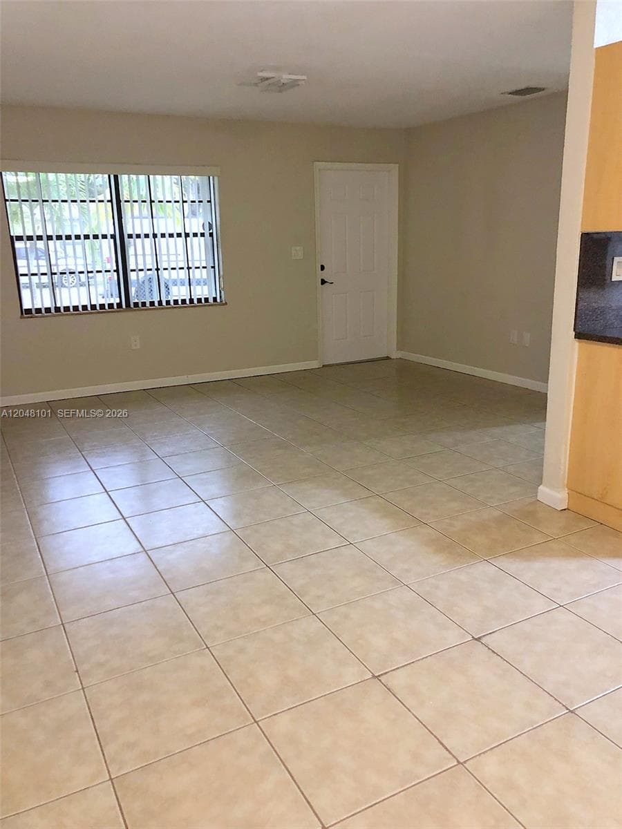 Neutral-toned interior space featuring ceramic tile flooring, a multi-pane window with horizontal blinds, and a solid-panel door