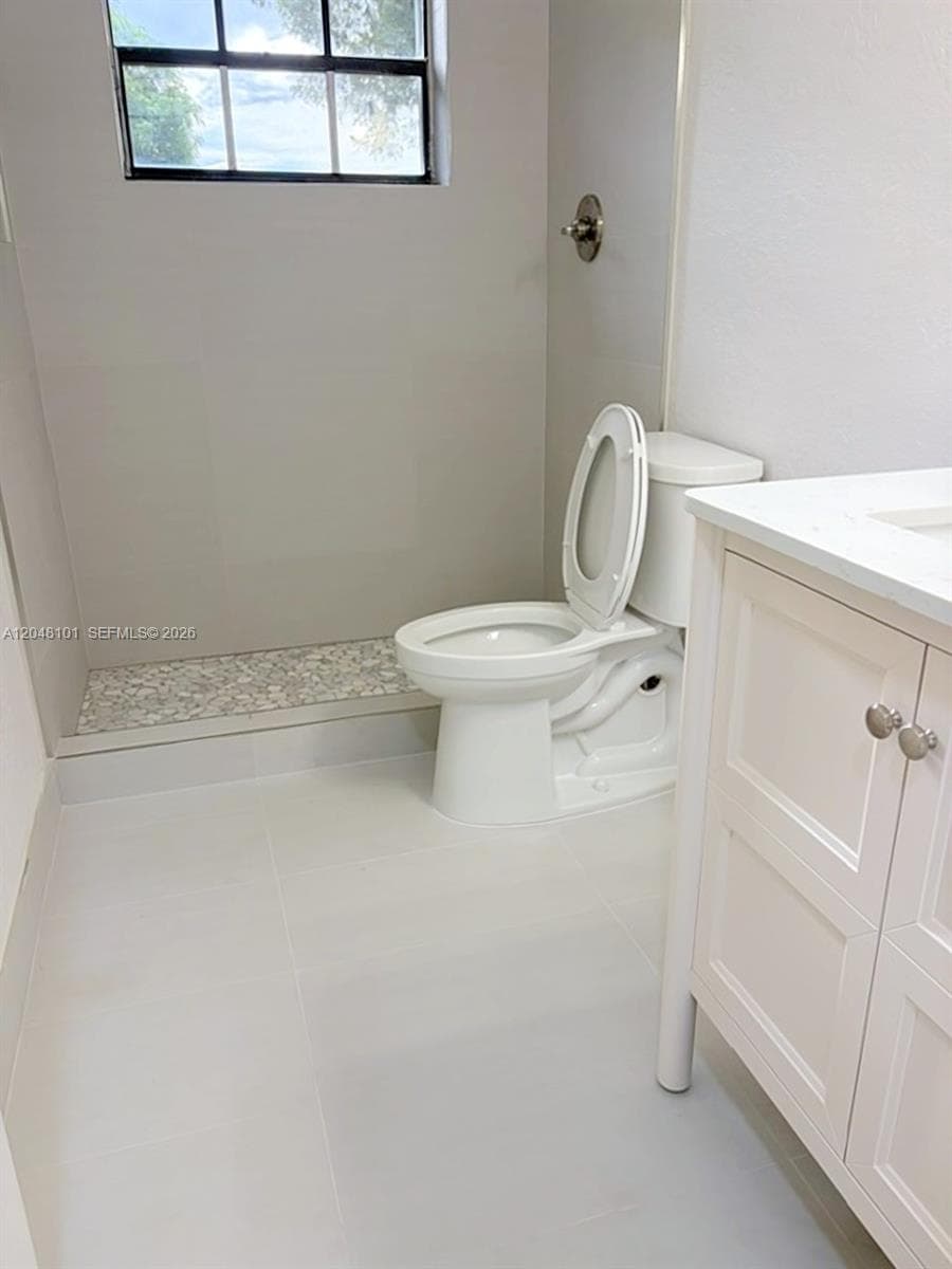Bathroom featuring a walk-in shower with stone pebble flooring, white cabinetry, a solid-surface countertop, and a window providing natural light