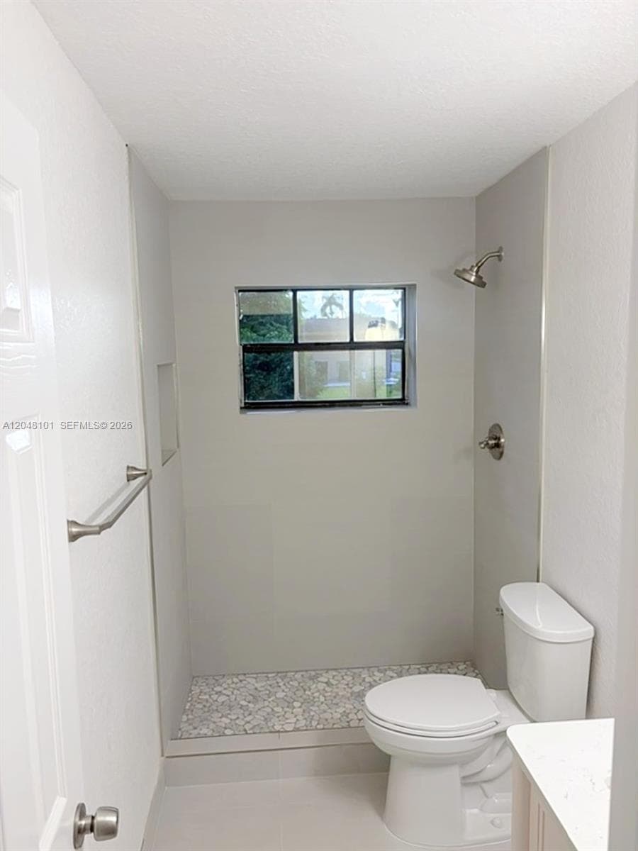 Shower featuring a pebble-stone floor, integrated wall-mounted shower head, built-in wall niche, window with black framing, and a metal towel bar