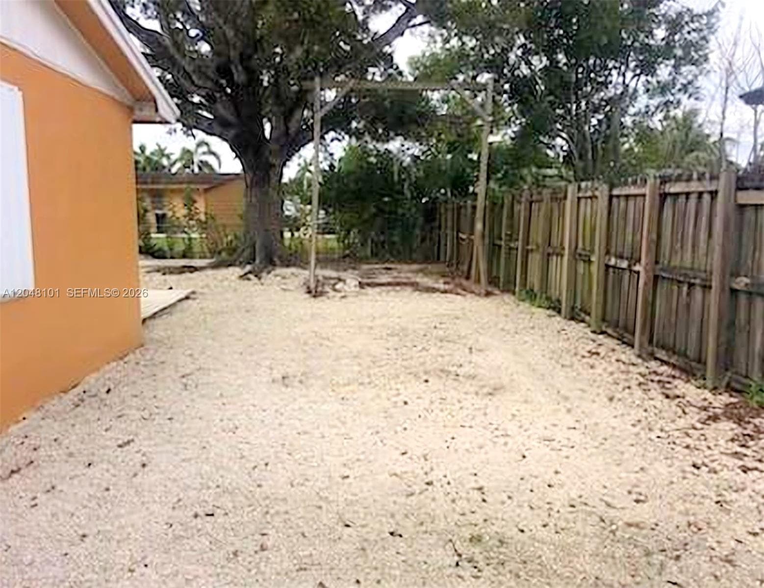 Backyard area featuring a gravel ground cover, mature tree, and wood-panel perimeter fencing