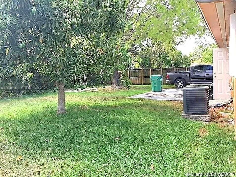 Backyard area featuring grass lawn, mature fruit-bearing tree, concrete patio, and wood privacy fencing