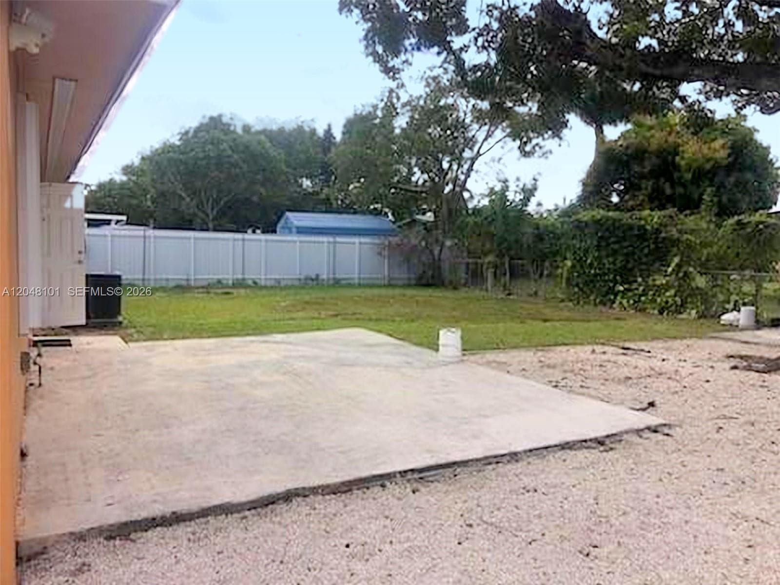 Rear exterior featuring a concrete patio, gravel ground cover, manicured lawn, and privacy fencing
