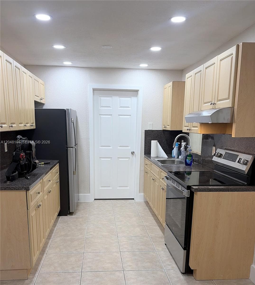 Kitchen featuring light-finish cabinetry, dark solid-surface countertops, recessed ceiling lighting, ceramic tile flooring, and stainless steel appliances