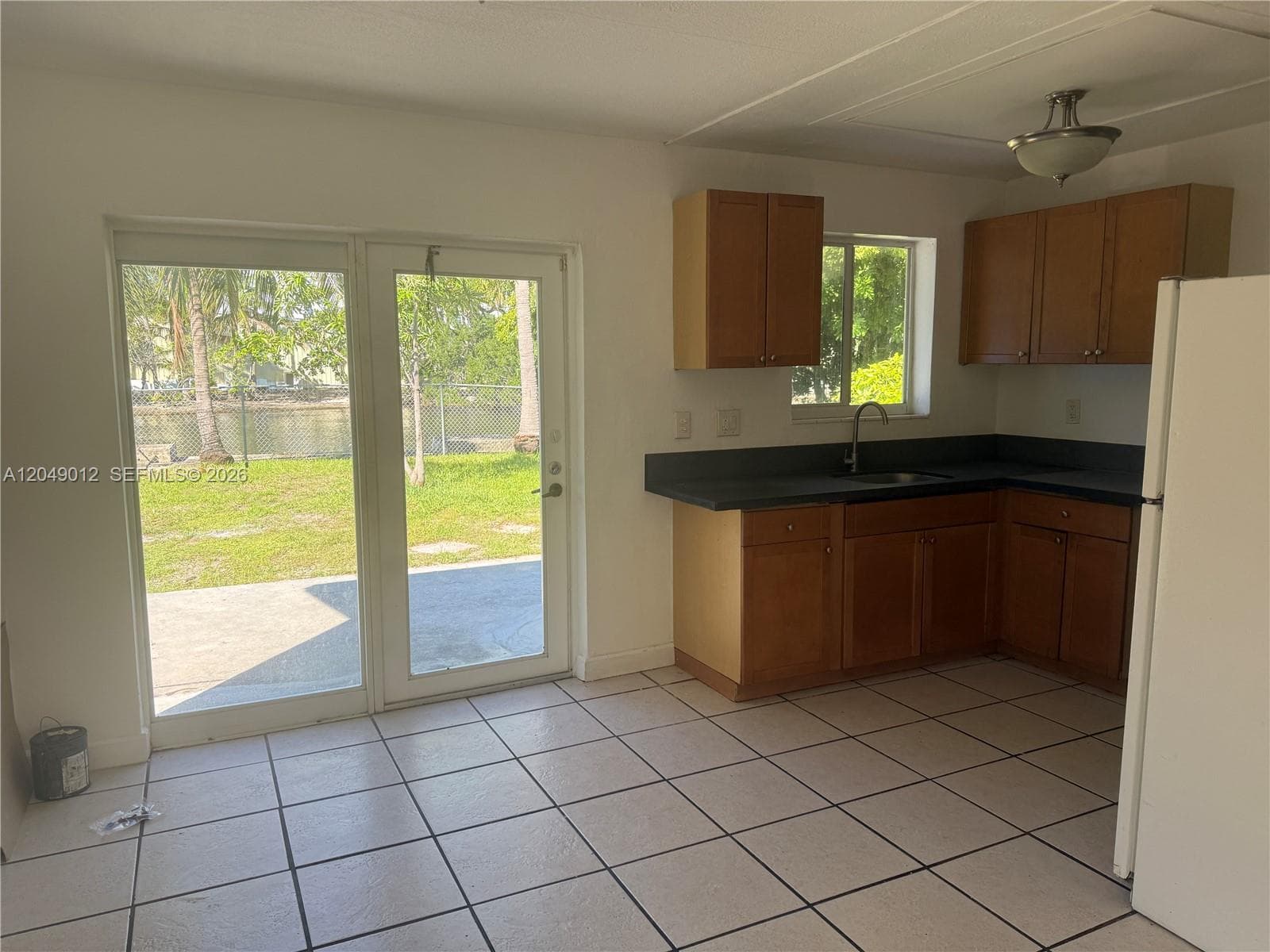 Kitchen featuring wood cabinetry, dark countertops, tile flooring, and glass-paneled sliding doors opening to a concrete patio and canal-front exterior