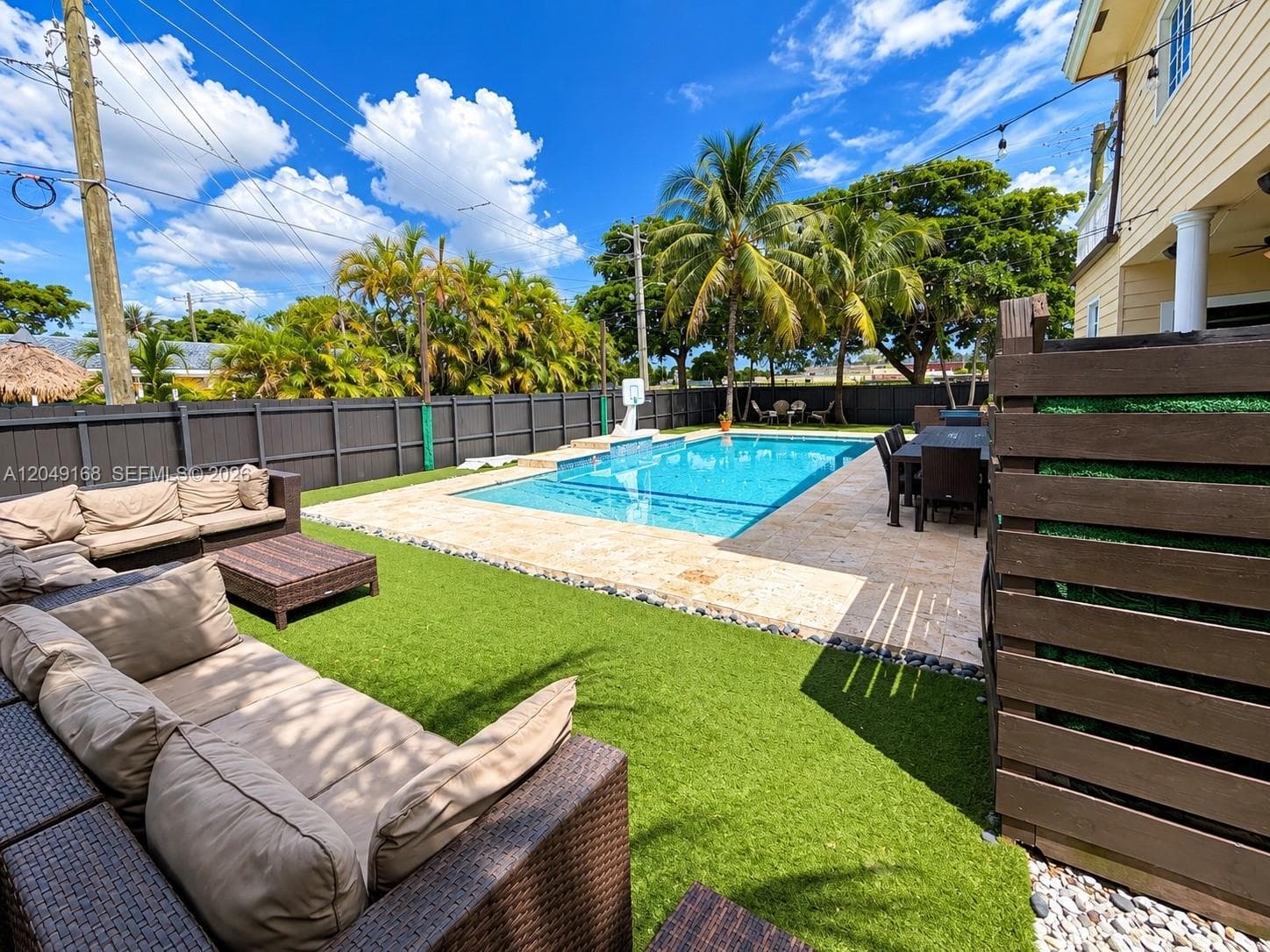 Private backyard featuring an inground swimming pool, stone-paver decking, synthetic turf lawn, and dark wood privacy fencing