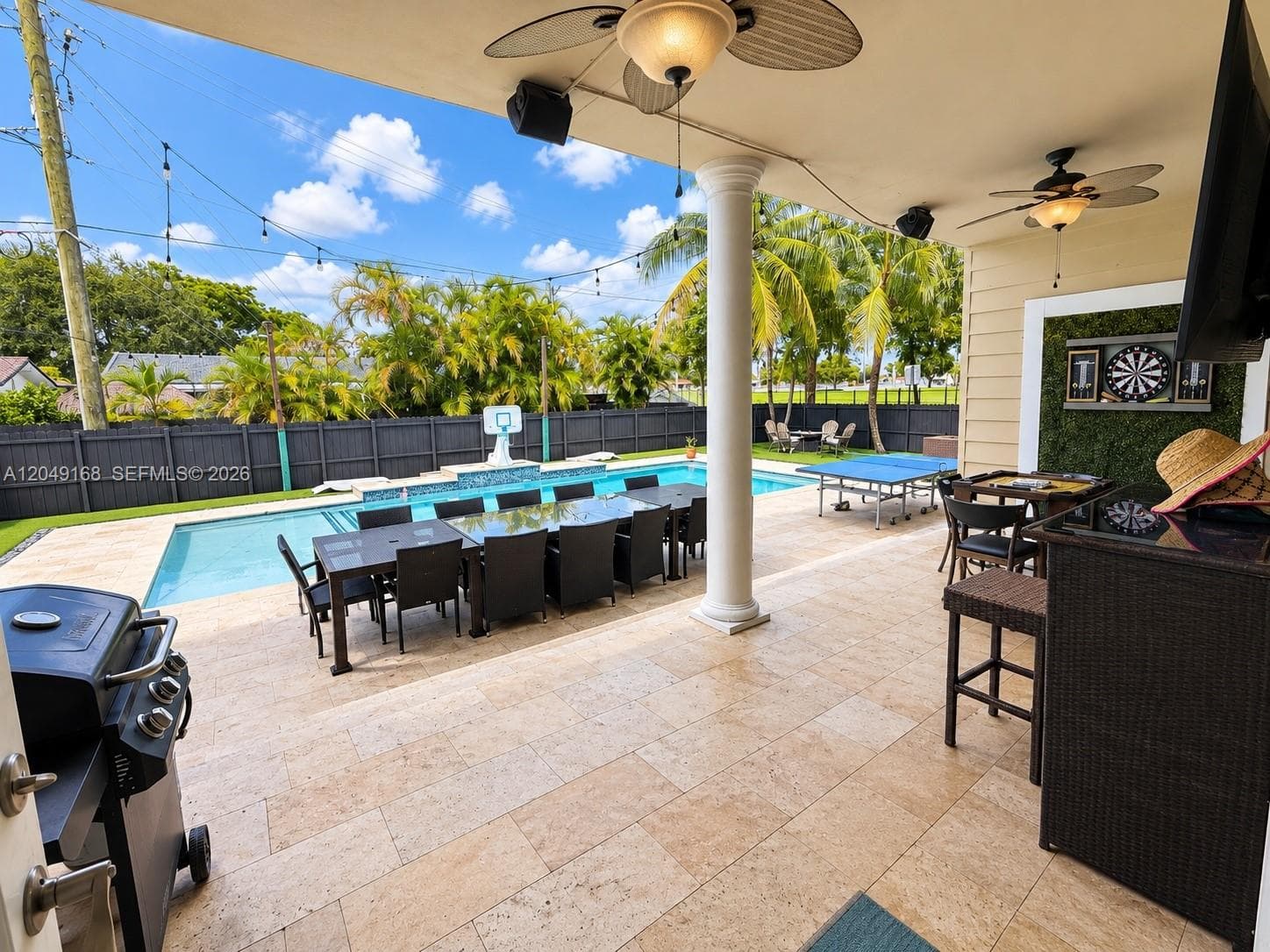 Covered outdoor patio featuring light-toned stone tile flooring, structural columns, ceiling-mounted fans, and integrated wall speakers