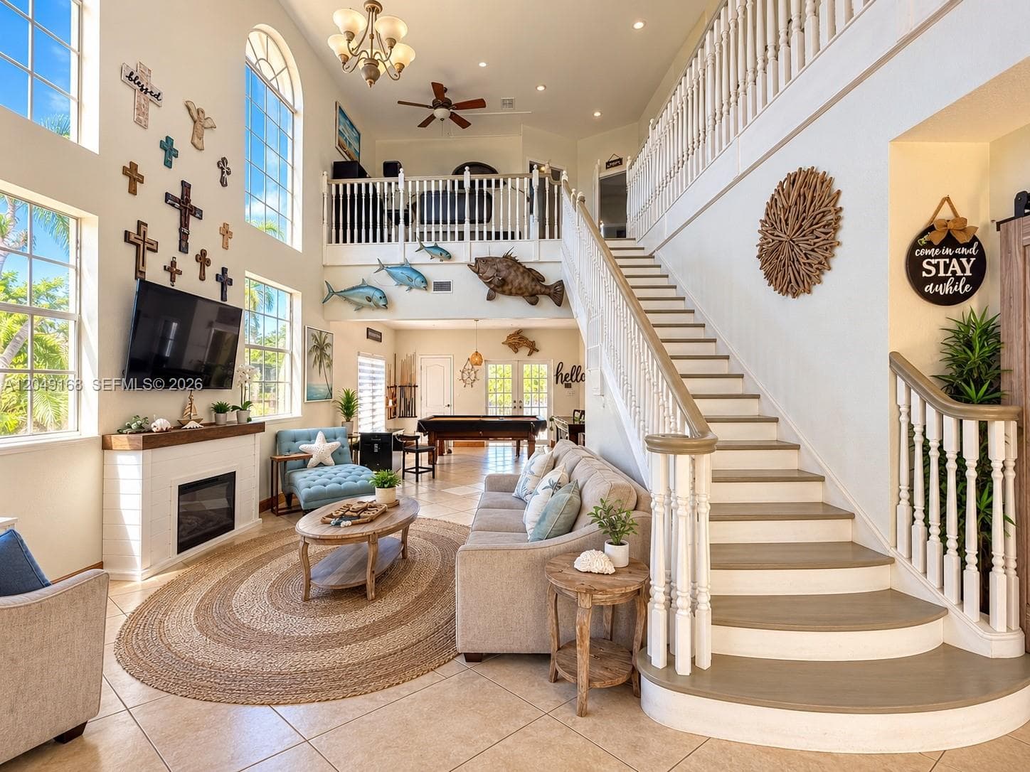 Grand double-height living area featuring vaulted ceilings, arched windows, a built-in fireplace with a wooden mantel, tiled flooring, and a staircase with decorative railings