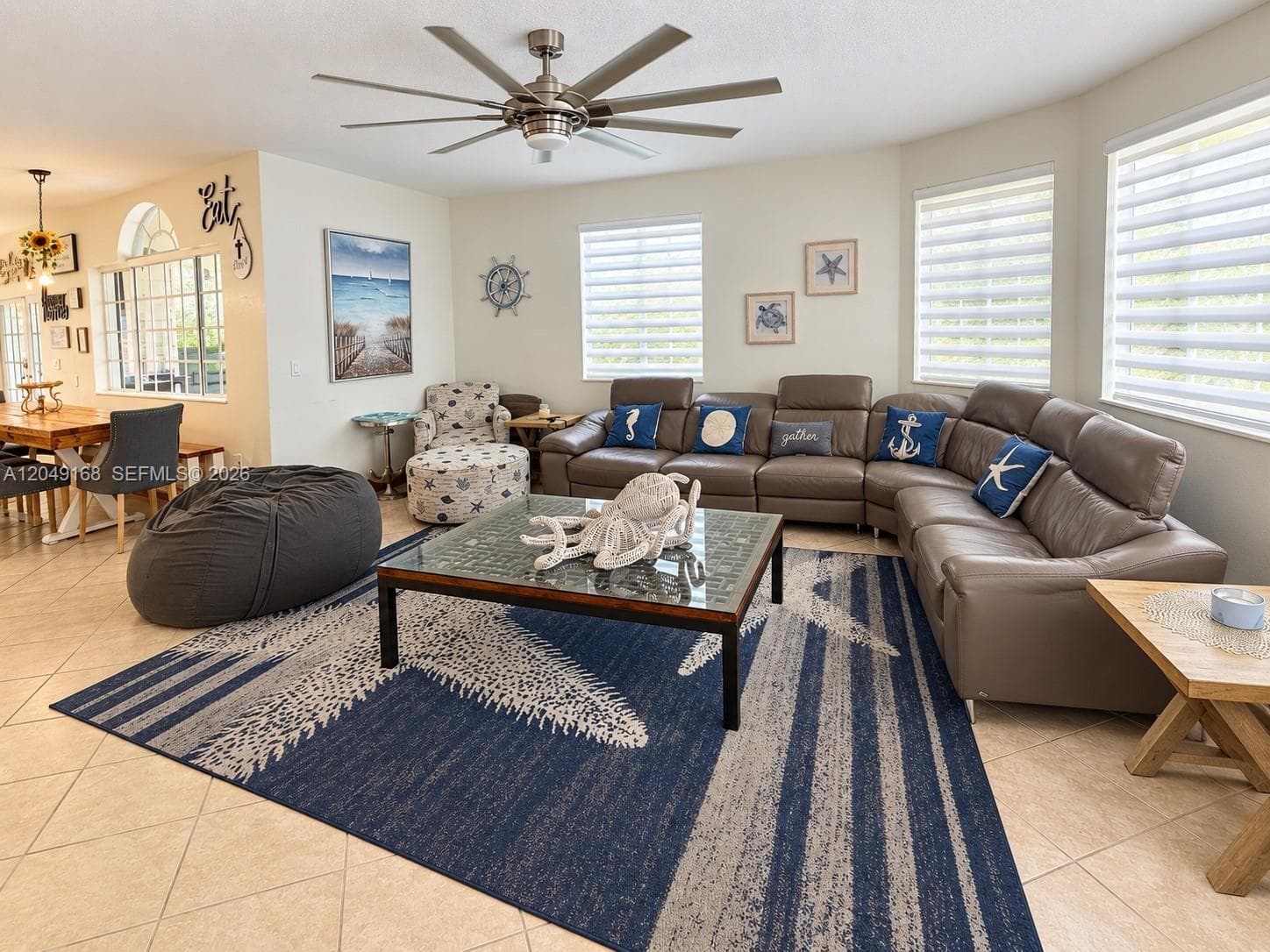 Spacious living area featuring large-format diagonal tile flooring, multi-blade ceiling fan, and oversized windows equipped with horizontal roller shades
