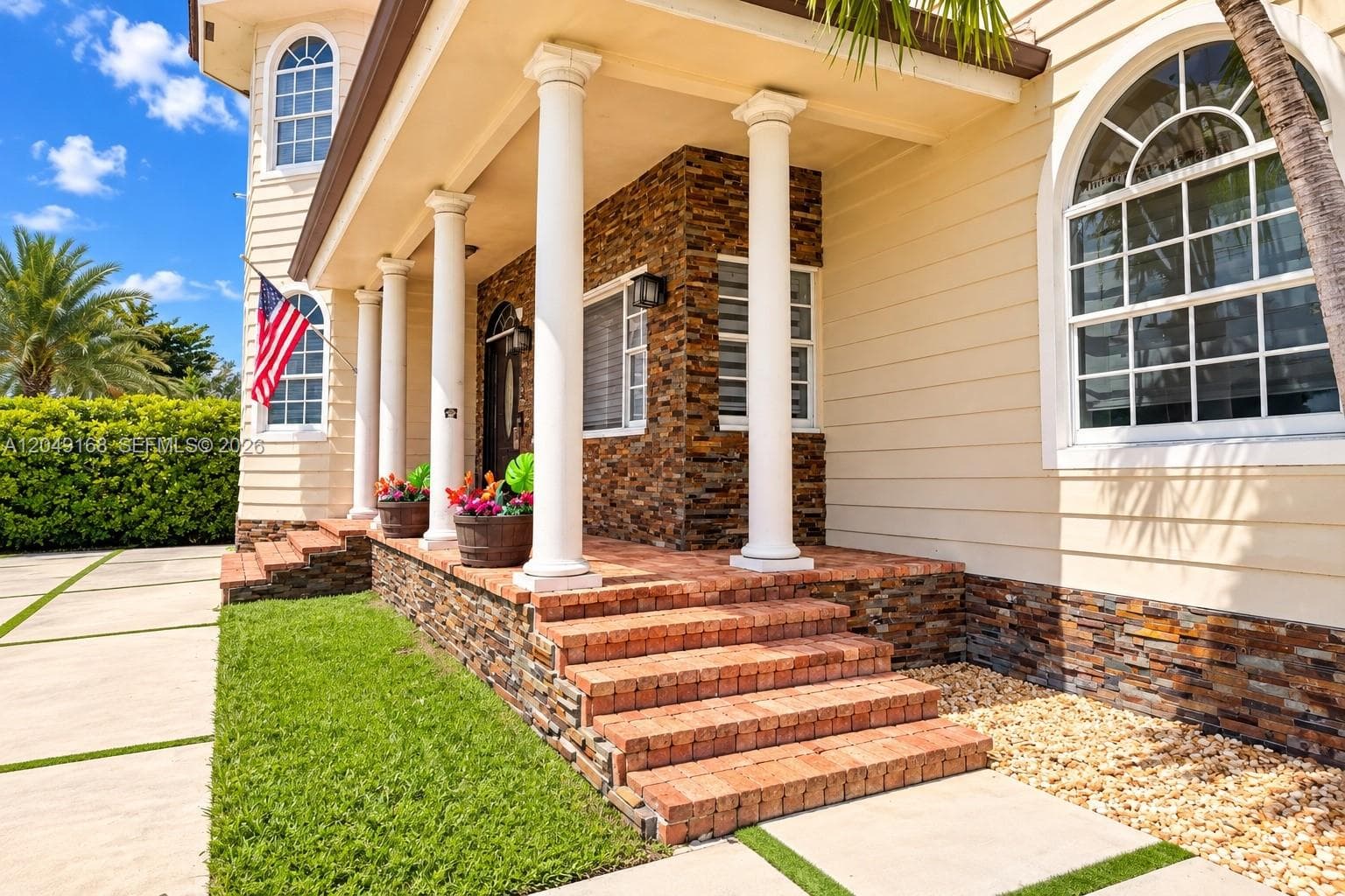 Covered front porch featuring stacked stone facade, decorative columns, arched windows, and brick steps
