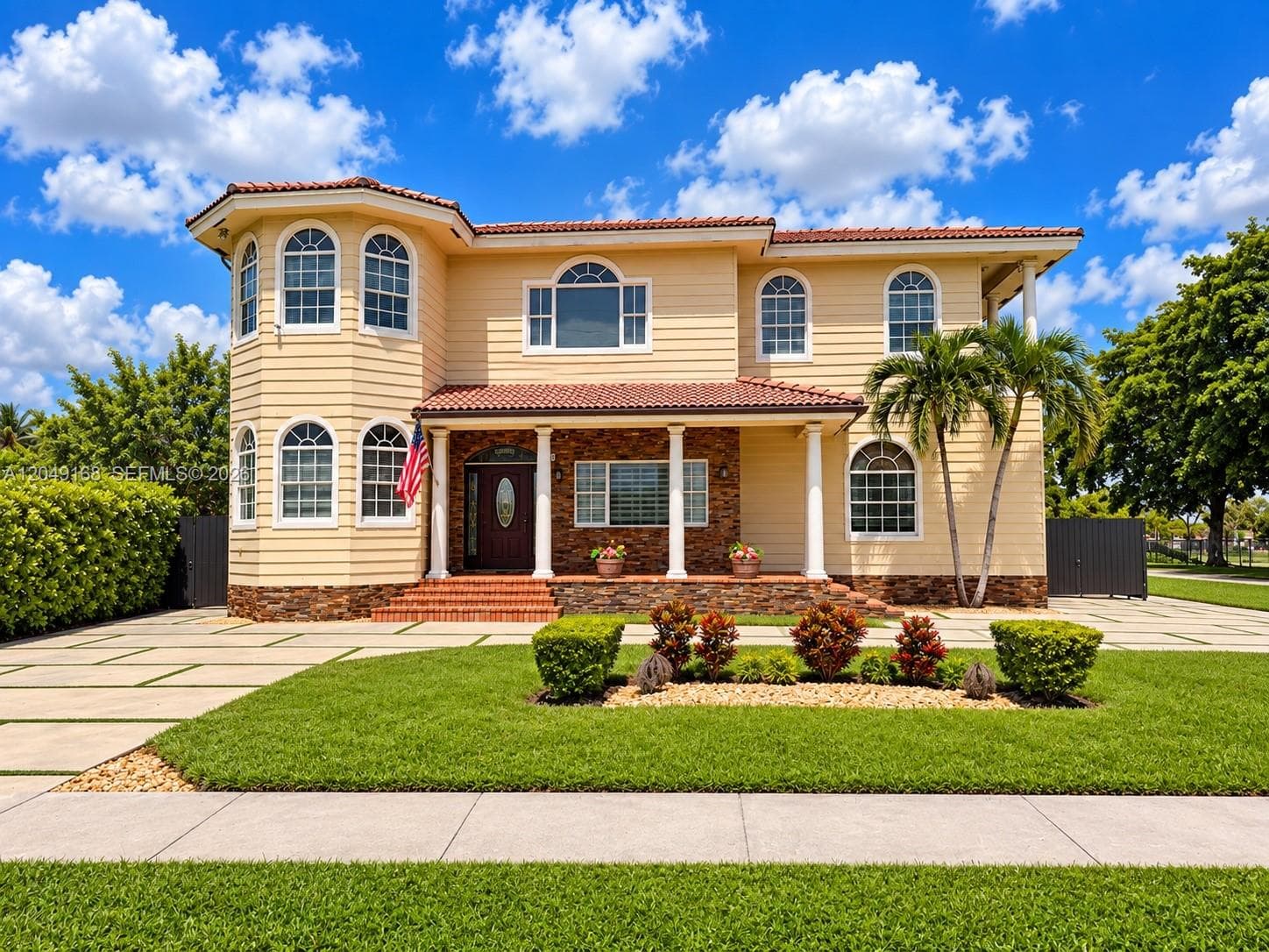 Two-story exterior featuring horizontal siding, a tile roof, arched windows, a covered front porch with columns, and a stone facade accent