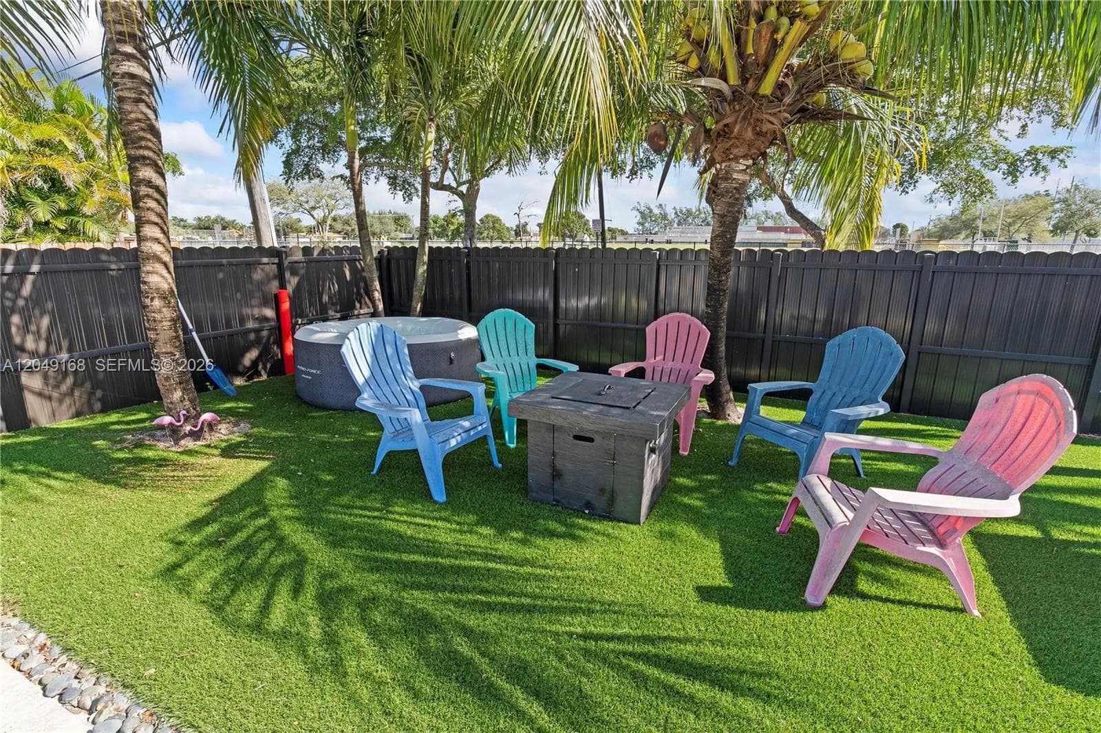 Enclosed outdoor space featuring synthetic turf, mature palm trees, and a dark-toned vertical privacy fence