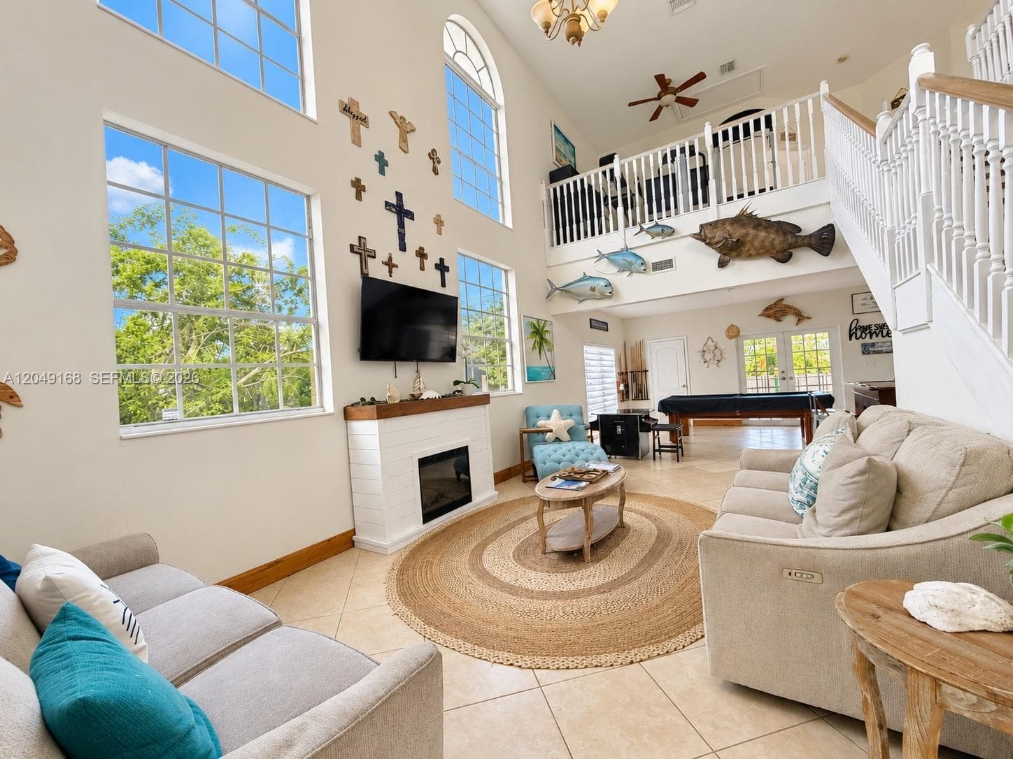 Double-height living area featuring large windows, a fireplace with a wood mantel, tile flooring, and a second-level balcony with a balustrade