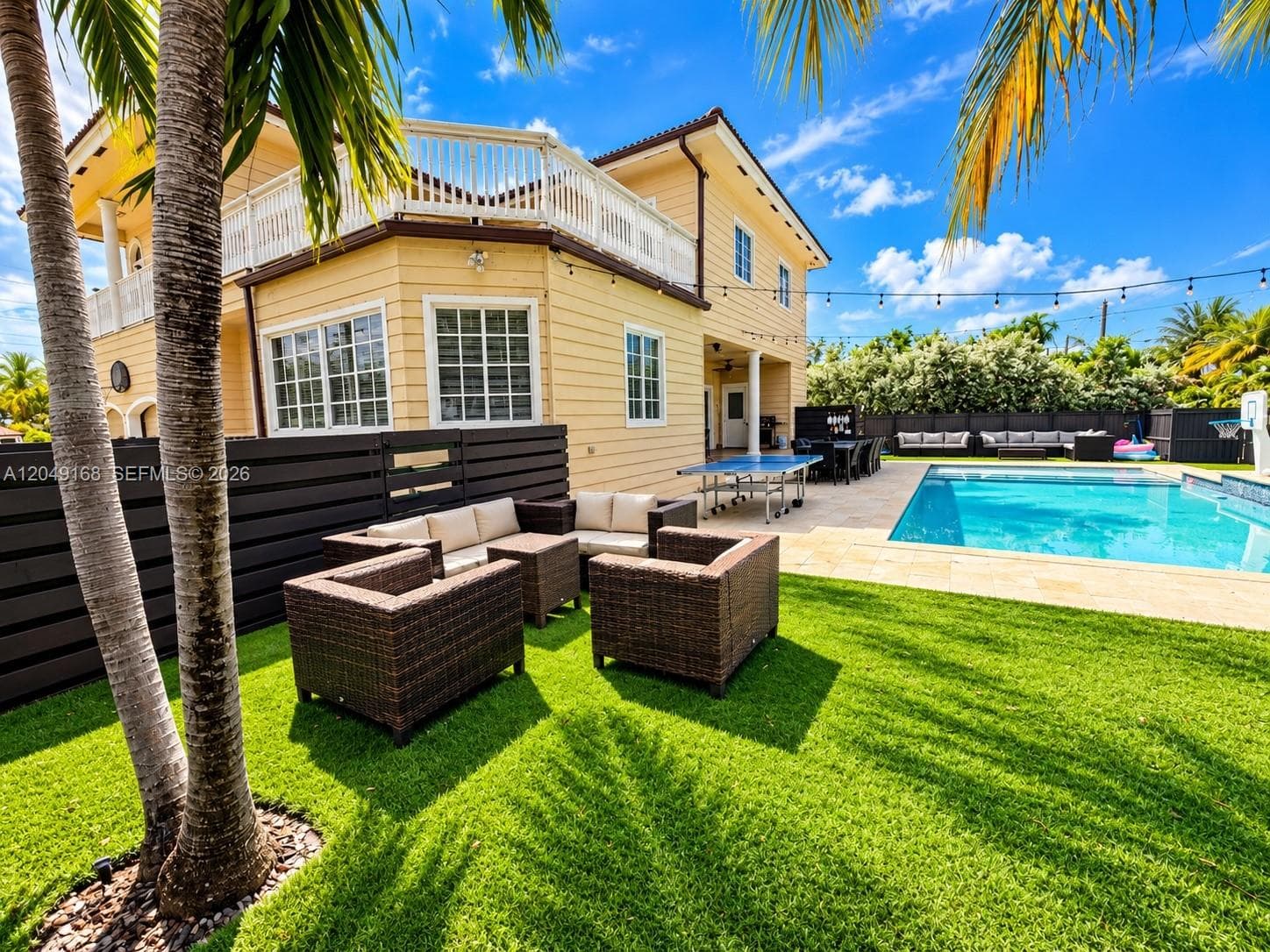 Exterior backyard space featuring a swimming pool, stone-paver pool deck, synthetic lawn, and a second-story wrap-around balcony with white railings