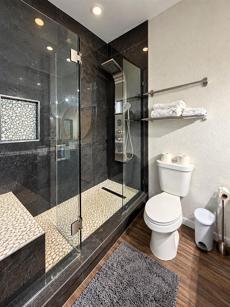 Walk-in shower featuring dark tile surround, integrated mosaic tile flooring, built-in bench, glass enclosure, and multi-jet shower panel