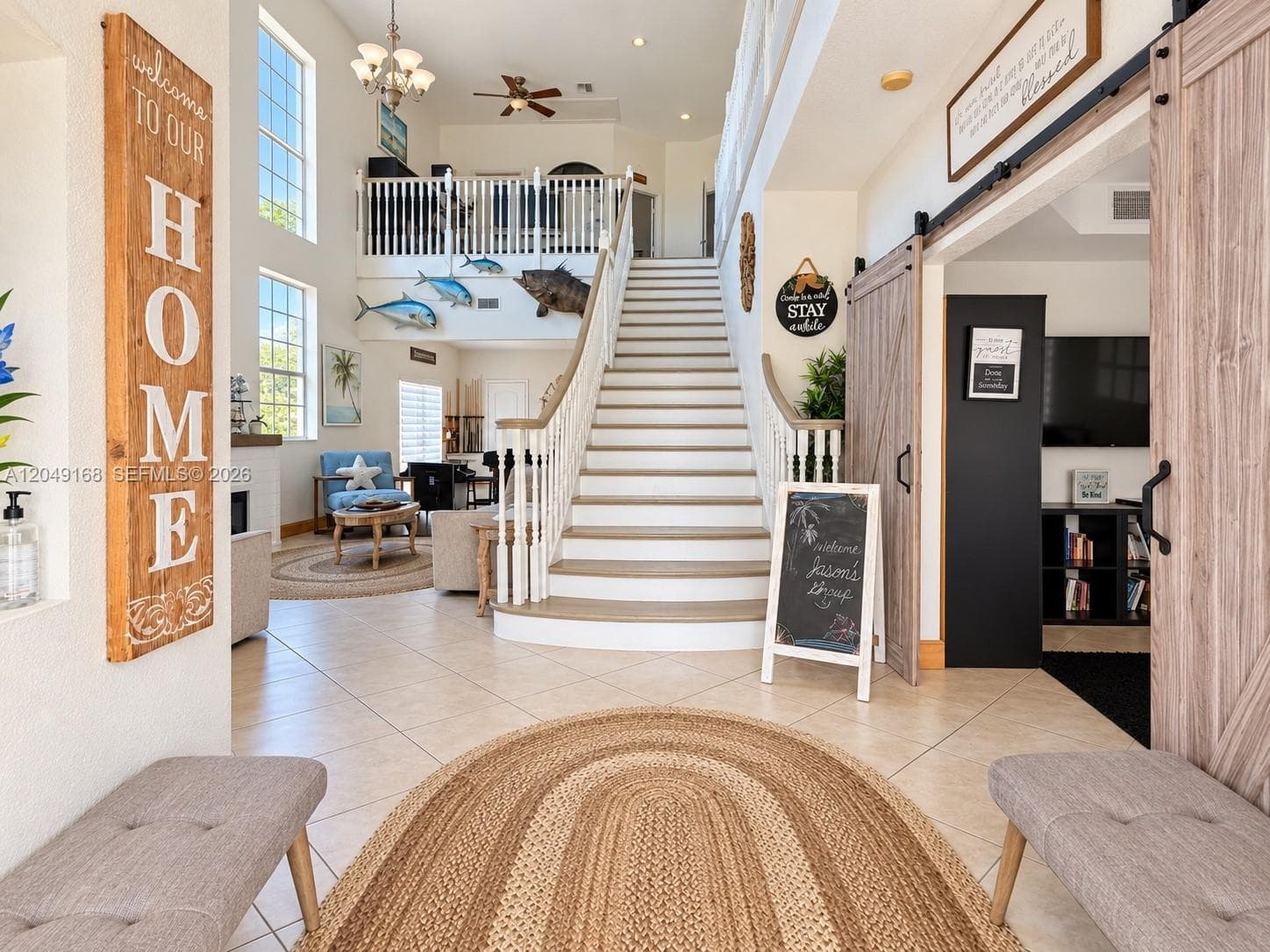 Two-story foyer featuring tile flooring, a central staircase with wood-finish treads and white balusters, multi-pane windows, and a sliding wood-finish barn door