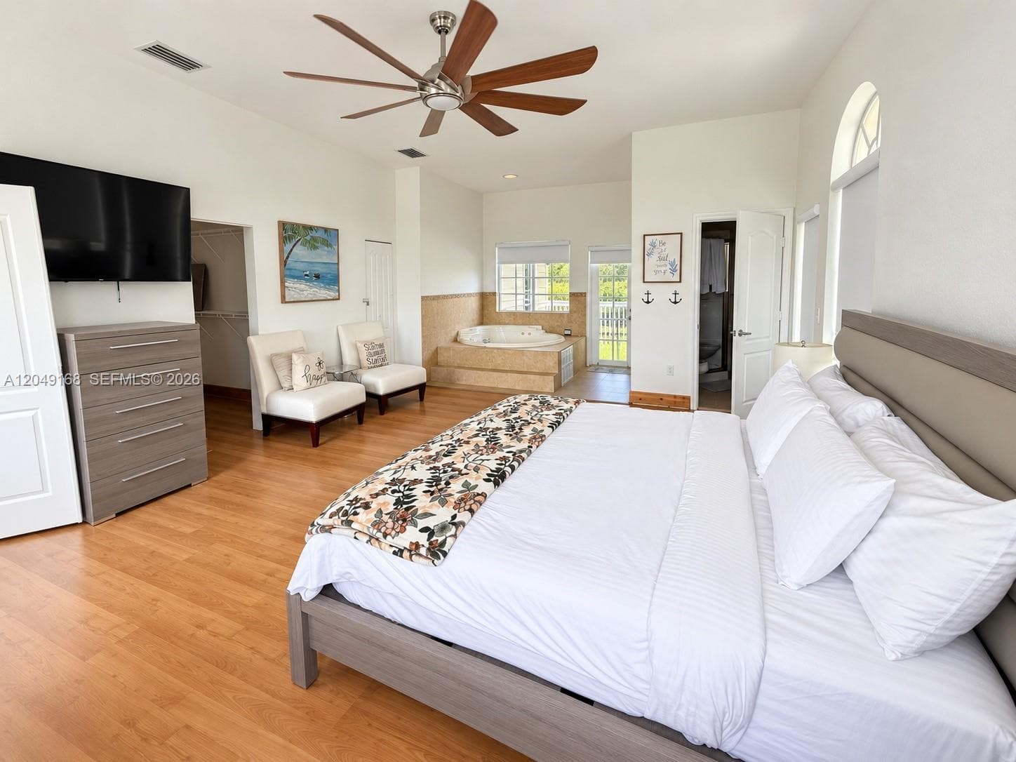 Spacious room featuring wood-finish flooring, vaulted ceilings, a multi-blade ceiling fan, a built-in jetted tub, and arched windows