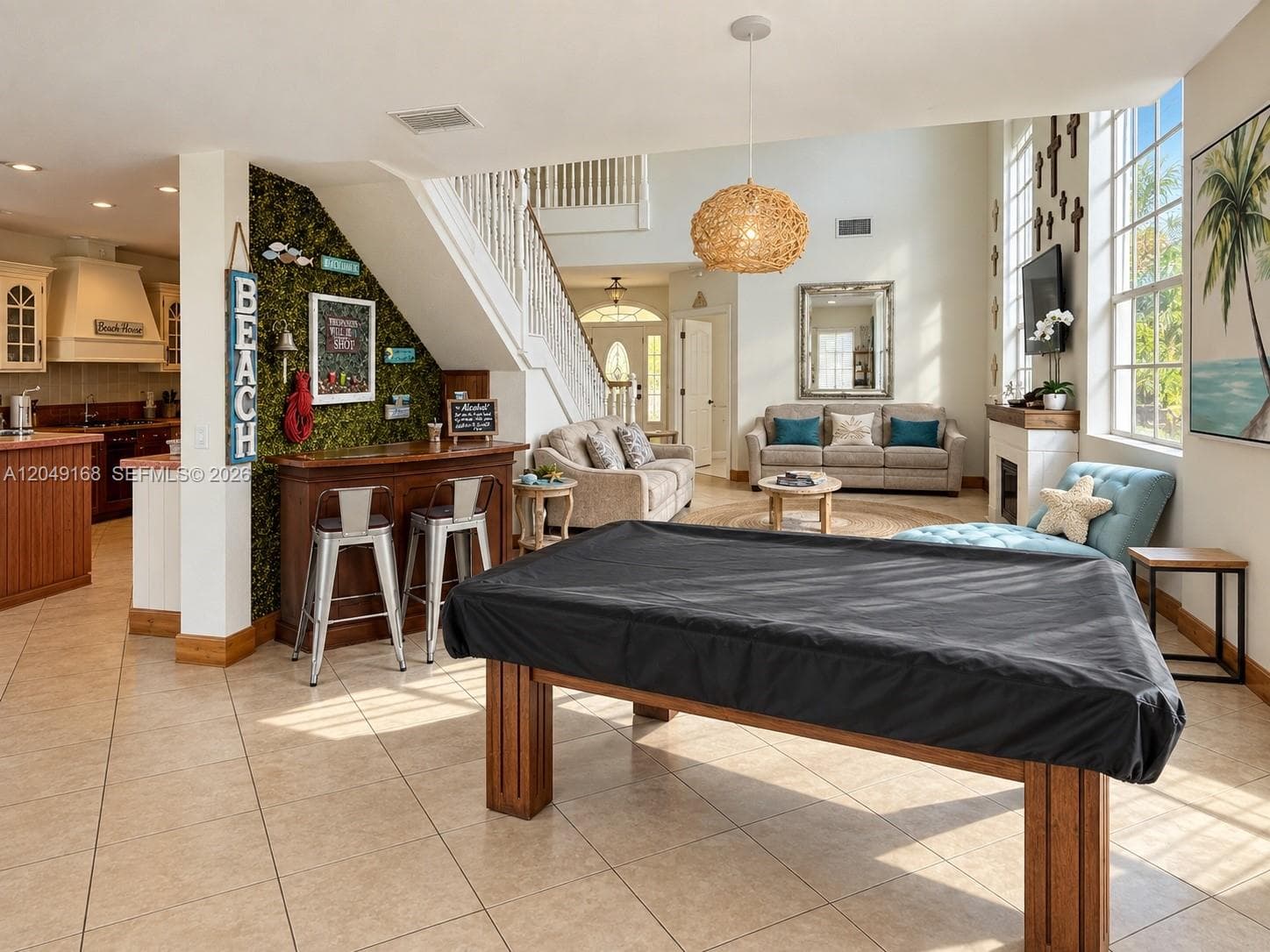 Open-concept floor plan featuring tile flooring, a staircase with white balusters, a fireplace with a mantel, and a built-in bar area with a textured accent wall