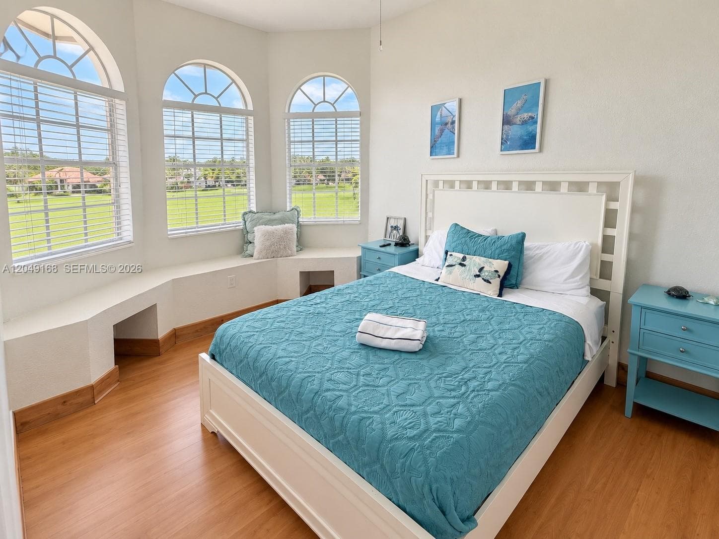 Bedroom featuring wood-finish flooring, three arched windows, and a built-in window bench