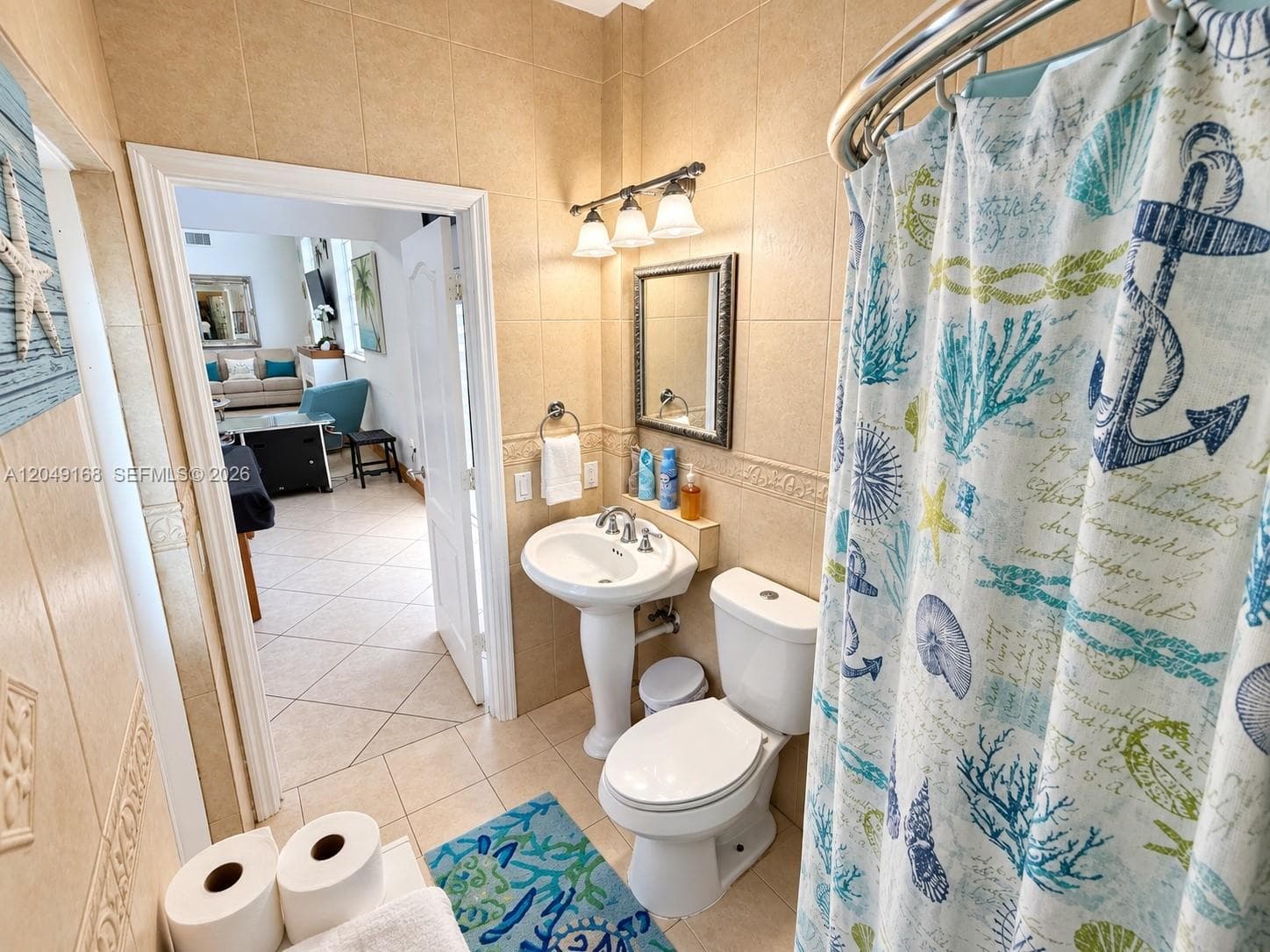 Full-height tile wall detailing, pedestal sink with dual-handle faucet, integrated wall mirror, and three-light vanity fixture