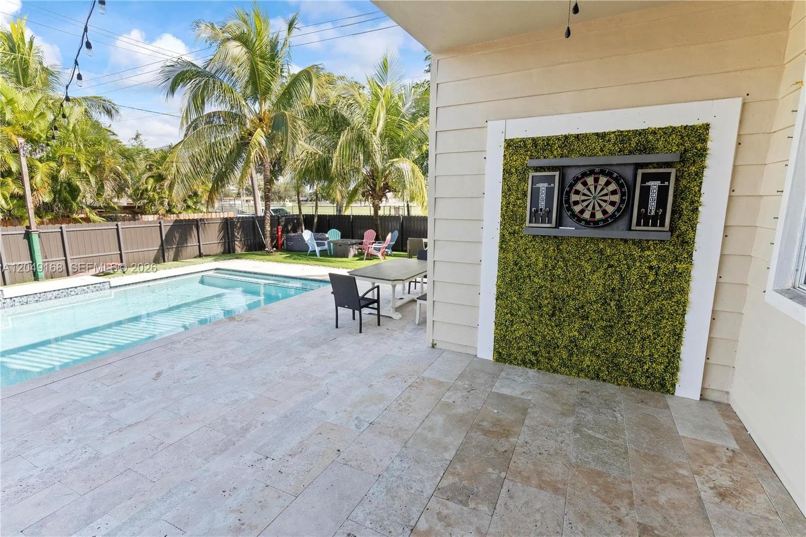 Covered patio featuring stone-tiled flooring, an integrated artificial hedge accent wall, a private swimming pool, and perimeter privacy fencing