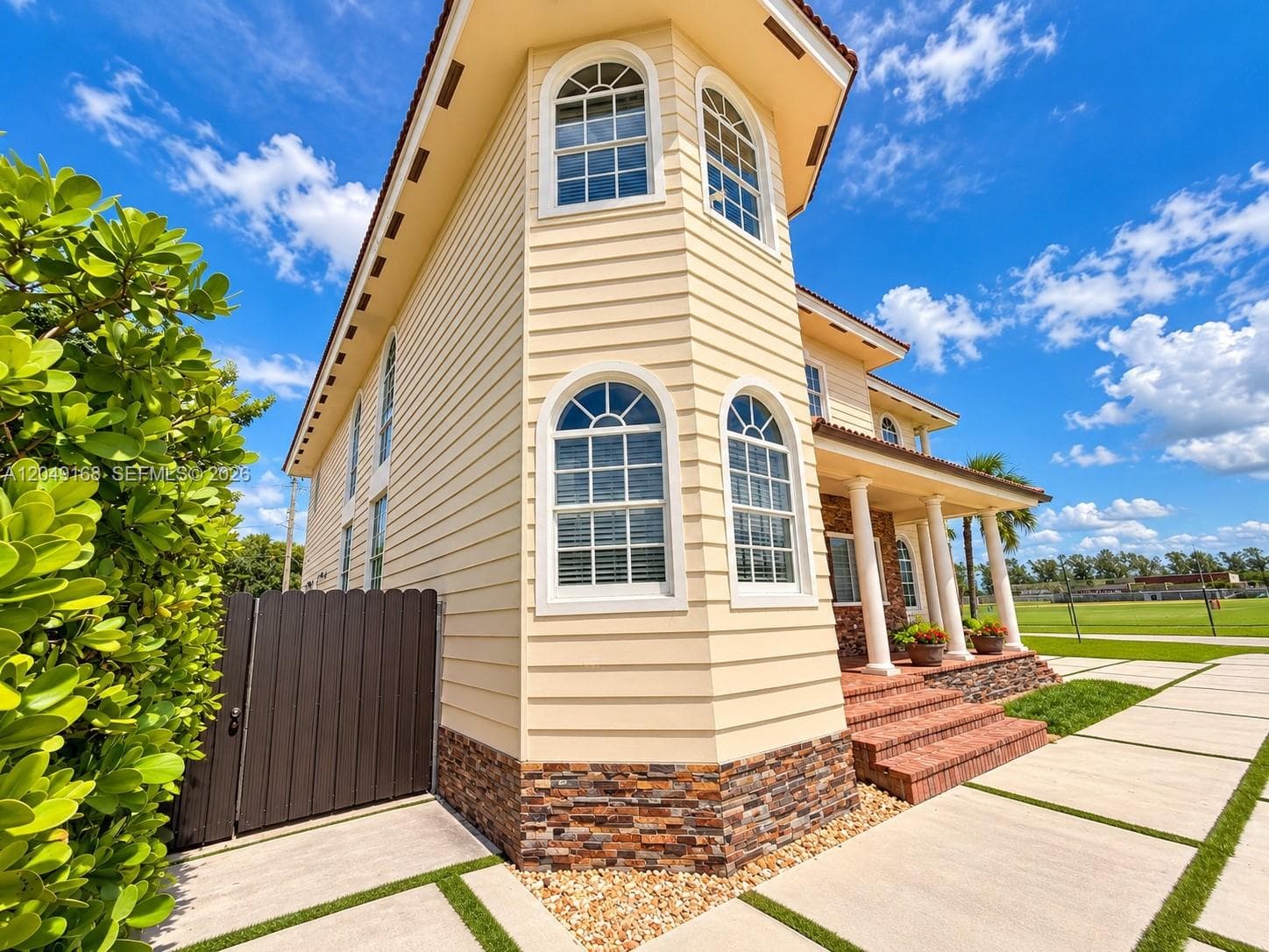 Exterior featuring light-toned horizontal siding, arched windows, stone veneer base, covered porch with classical columns, and multi-level brick steps