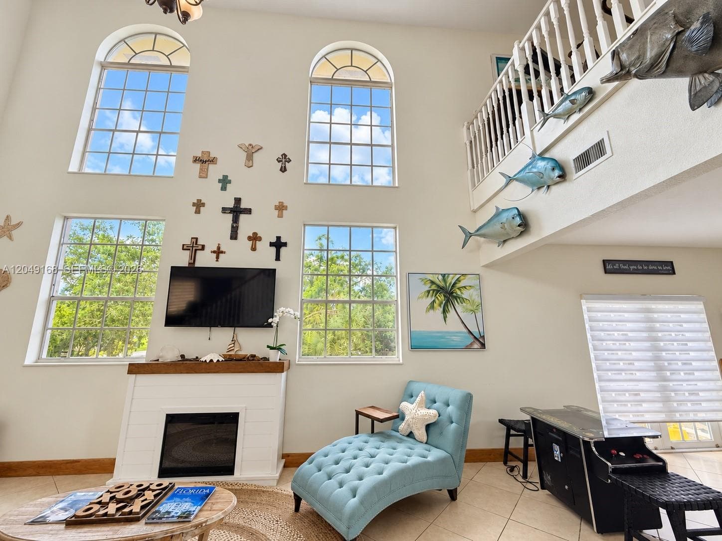Double-height ceiling, four arched windows with grid detailing, fireplace with white shiplap-style surround and wood mantel, and a staircase with white balusters